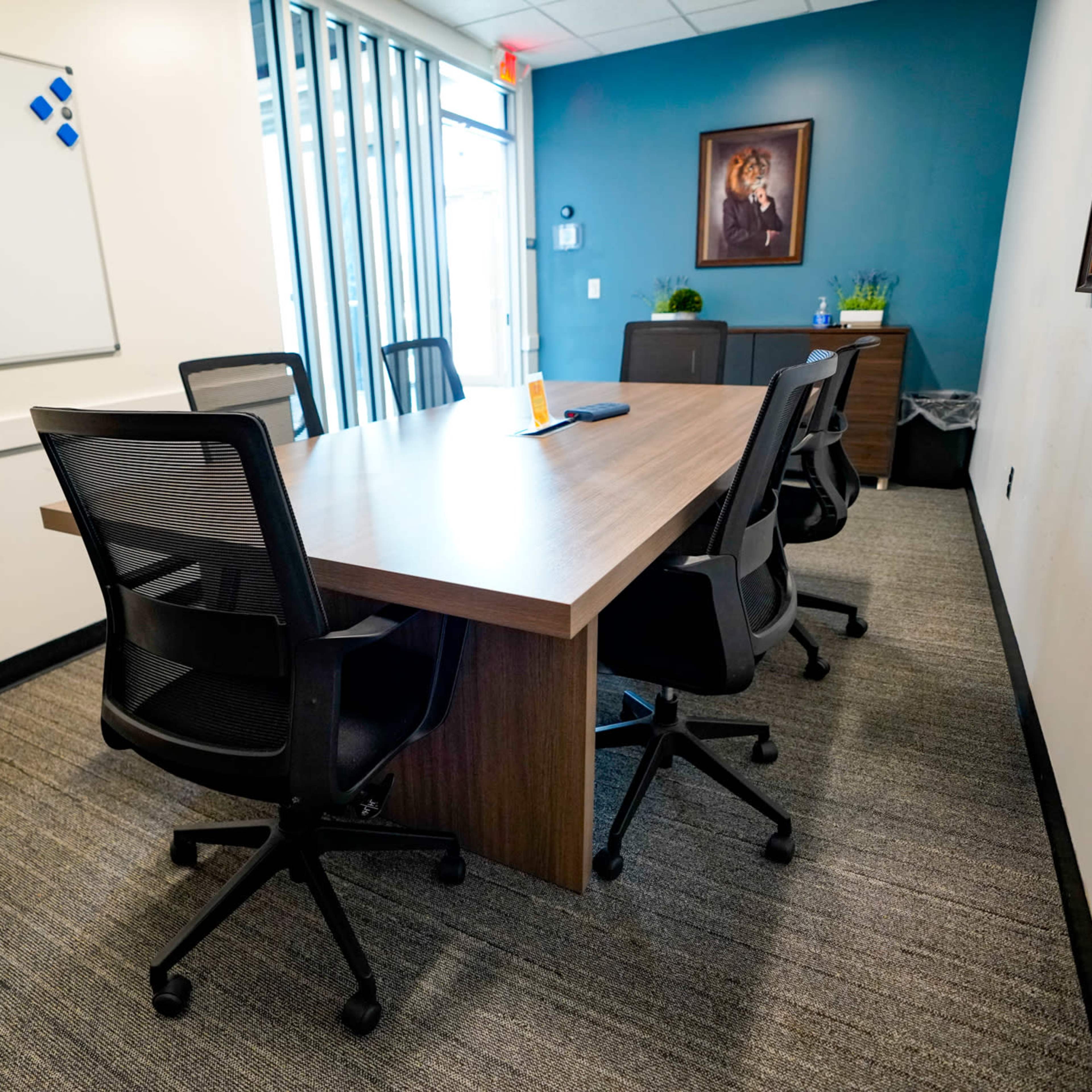A conference room with a large wooden table surrounded by black ergonomic chairs and a whiteboard on one wall.