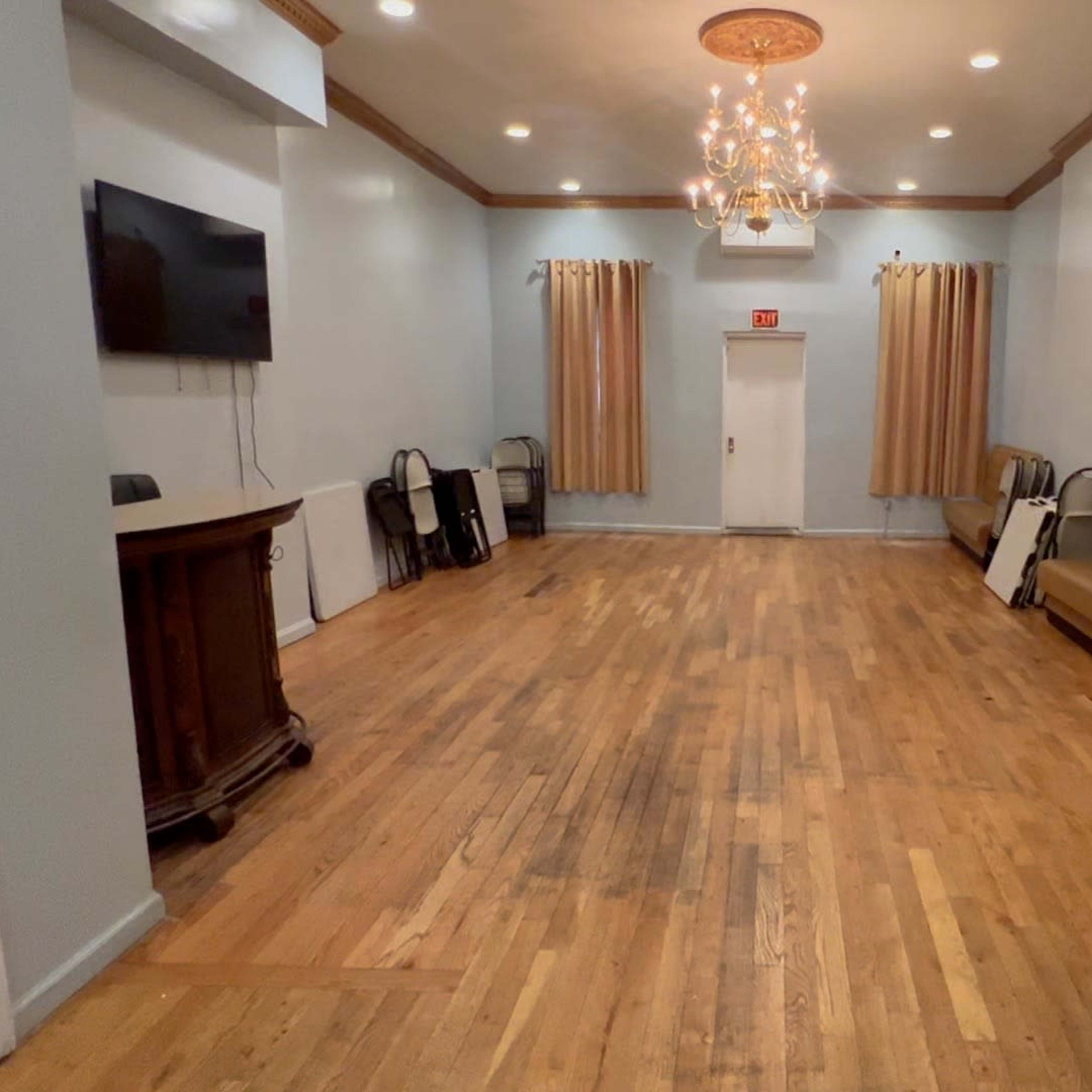 An empty room with wooden flooring, a chandelier, and decorative walls, featuring a bar area and seating along the sides.