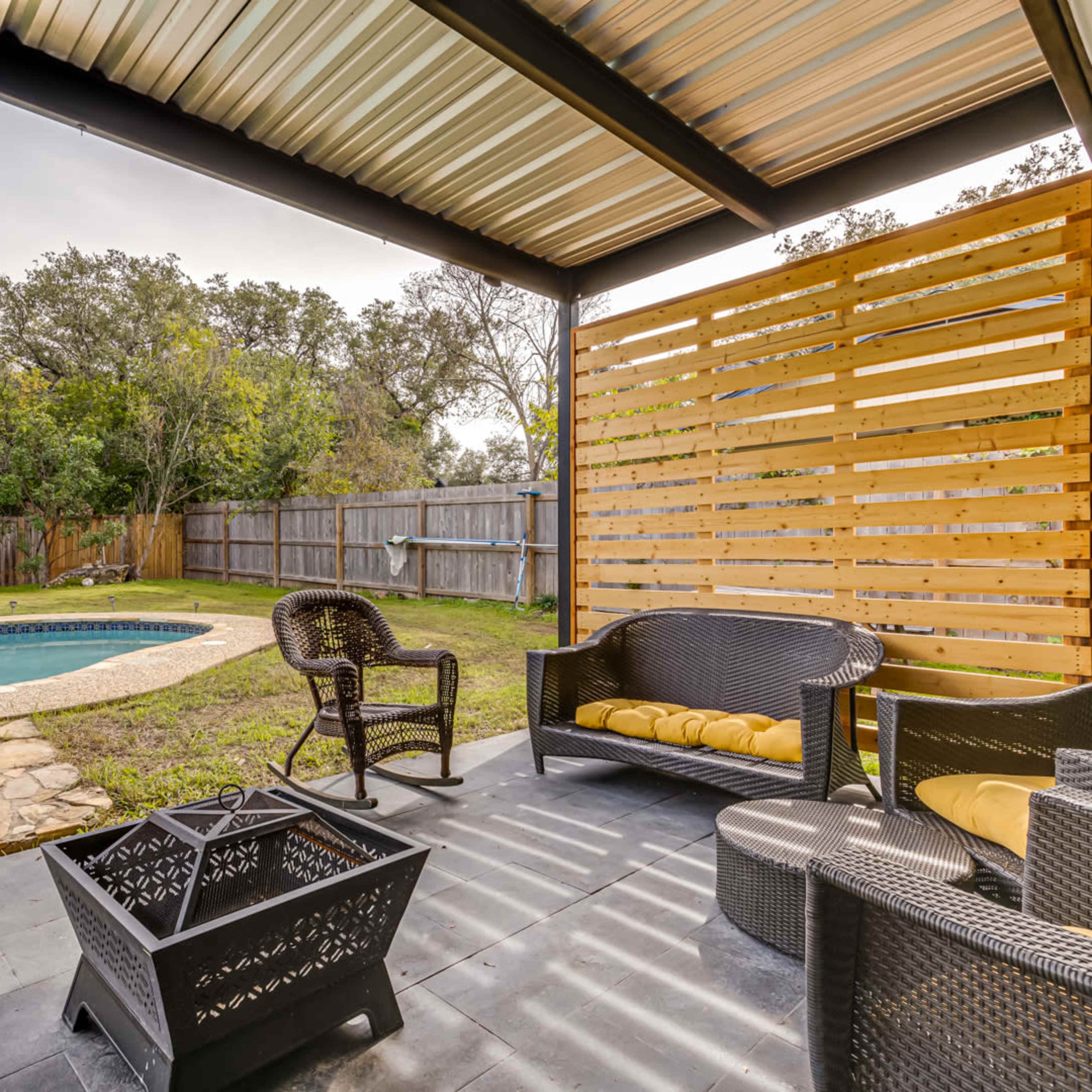 A backyard patio area with a pool, slide, and a seating arrangement featuring wicker furniture and a fire pit.