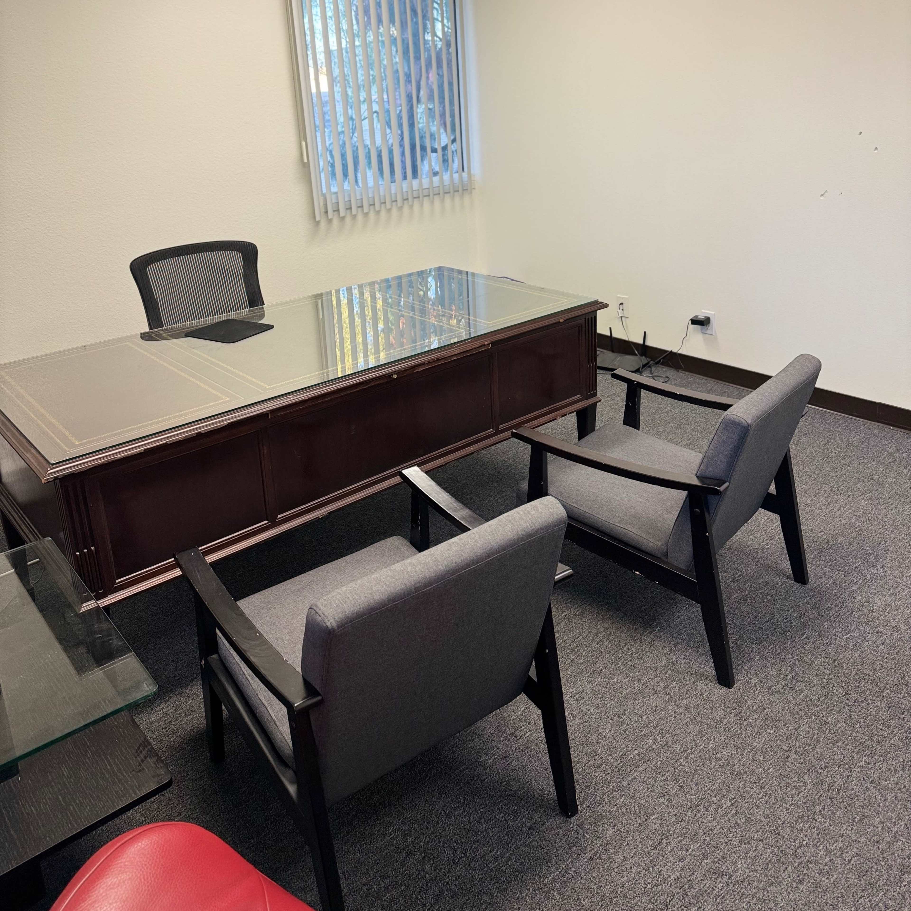 A small office with a large desk, two gray chairs in front of it, and vertical blinds on a window.