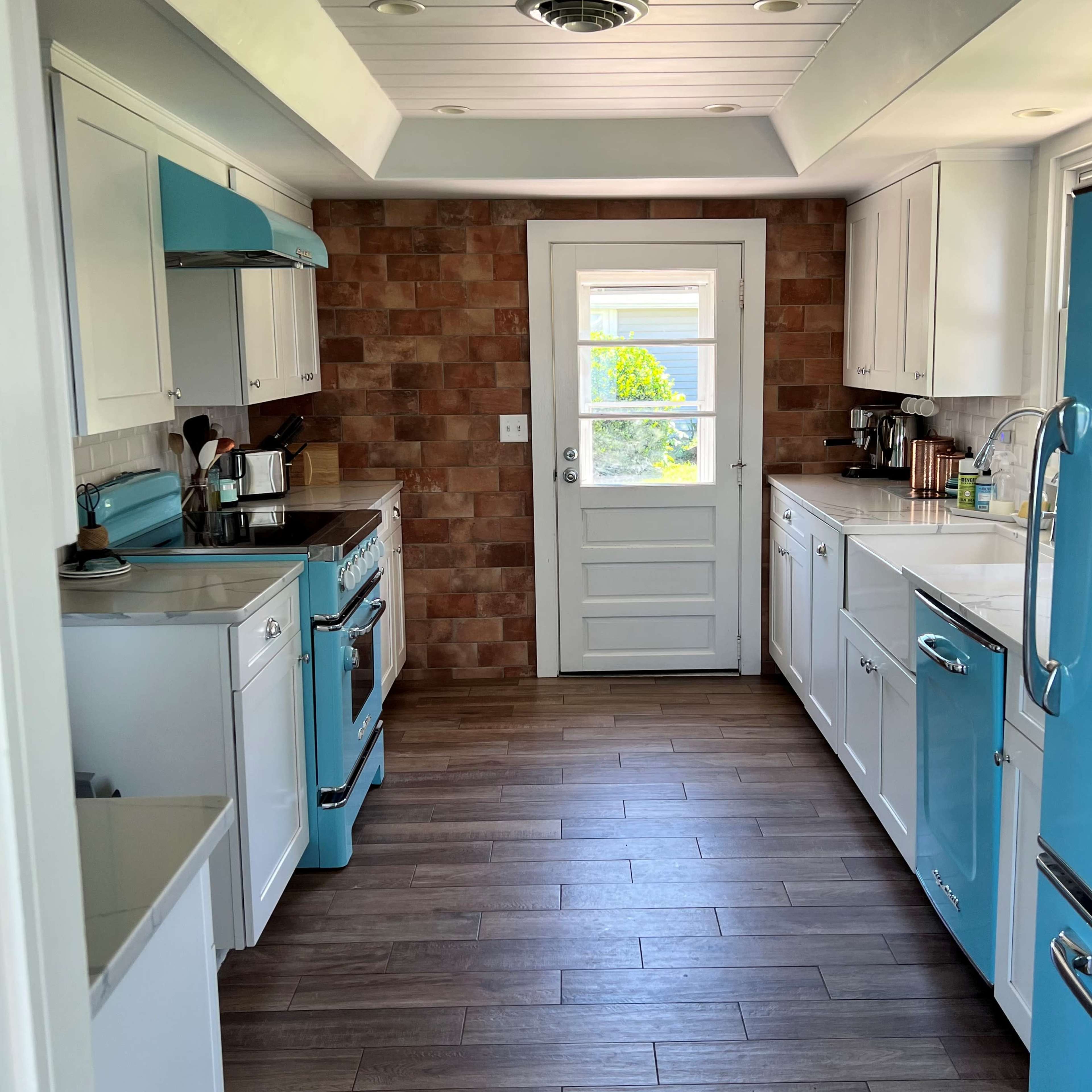 A modern kitchen featuring blue appliances, white cabinets, and a door leading to the outside.