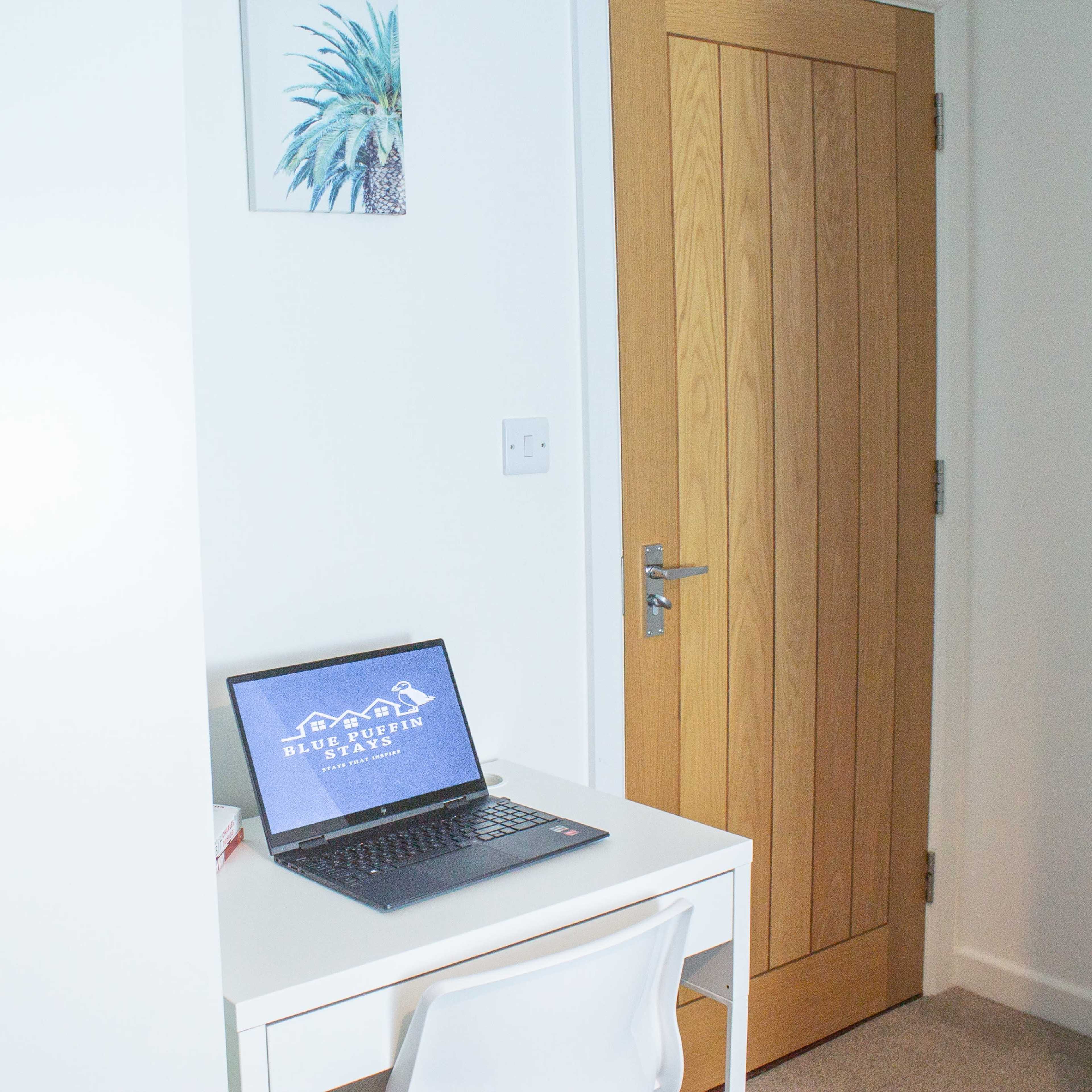 A small workspace featuring a laptop on a white desk beside a closed wooden door and a closet.