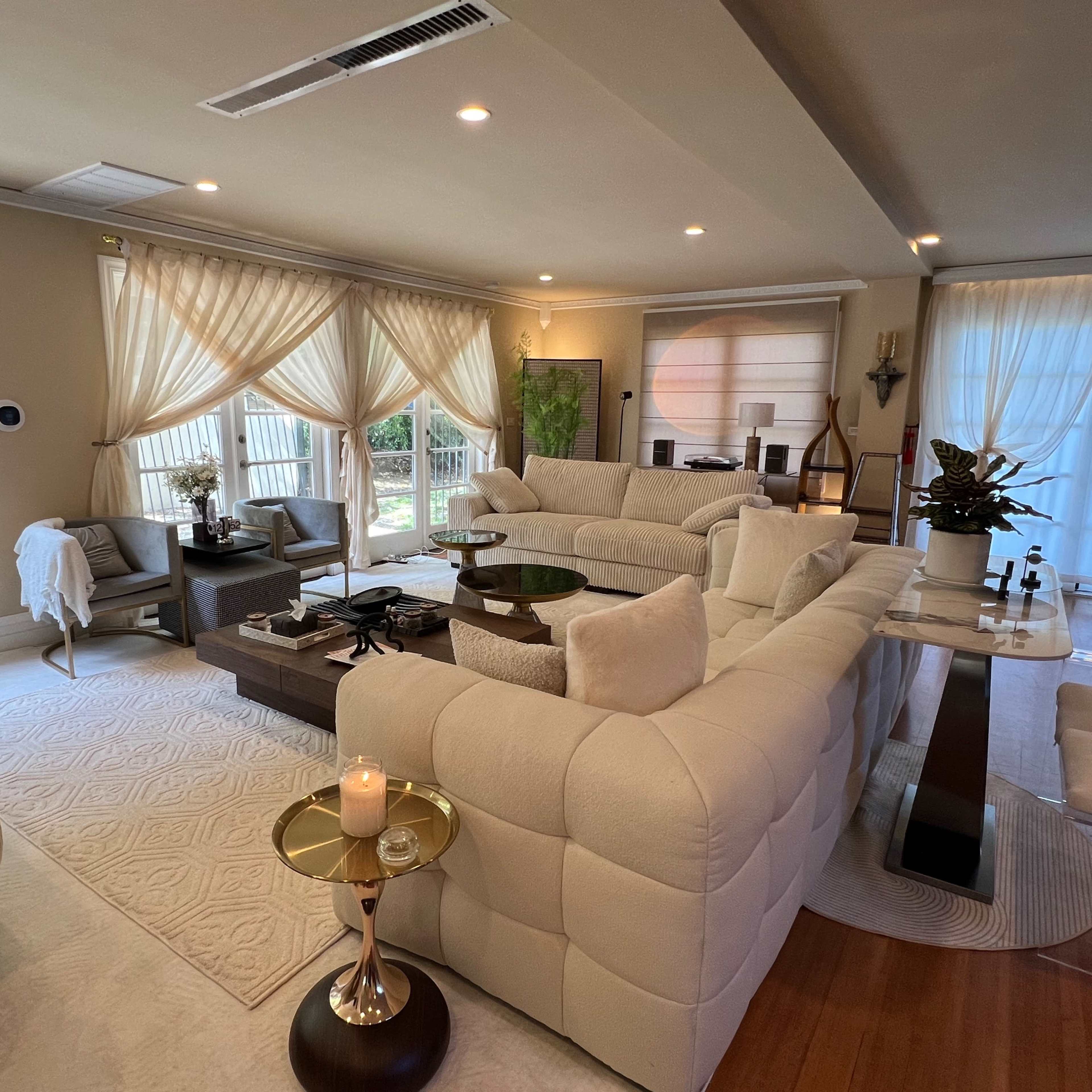The living room features a large, white sectional sofa, a glass coffee table, and large windows with sheer curtains, creating a bright and open space.