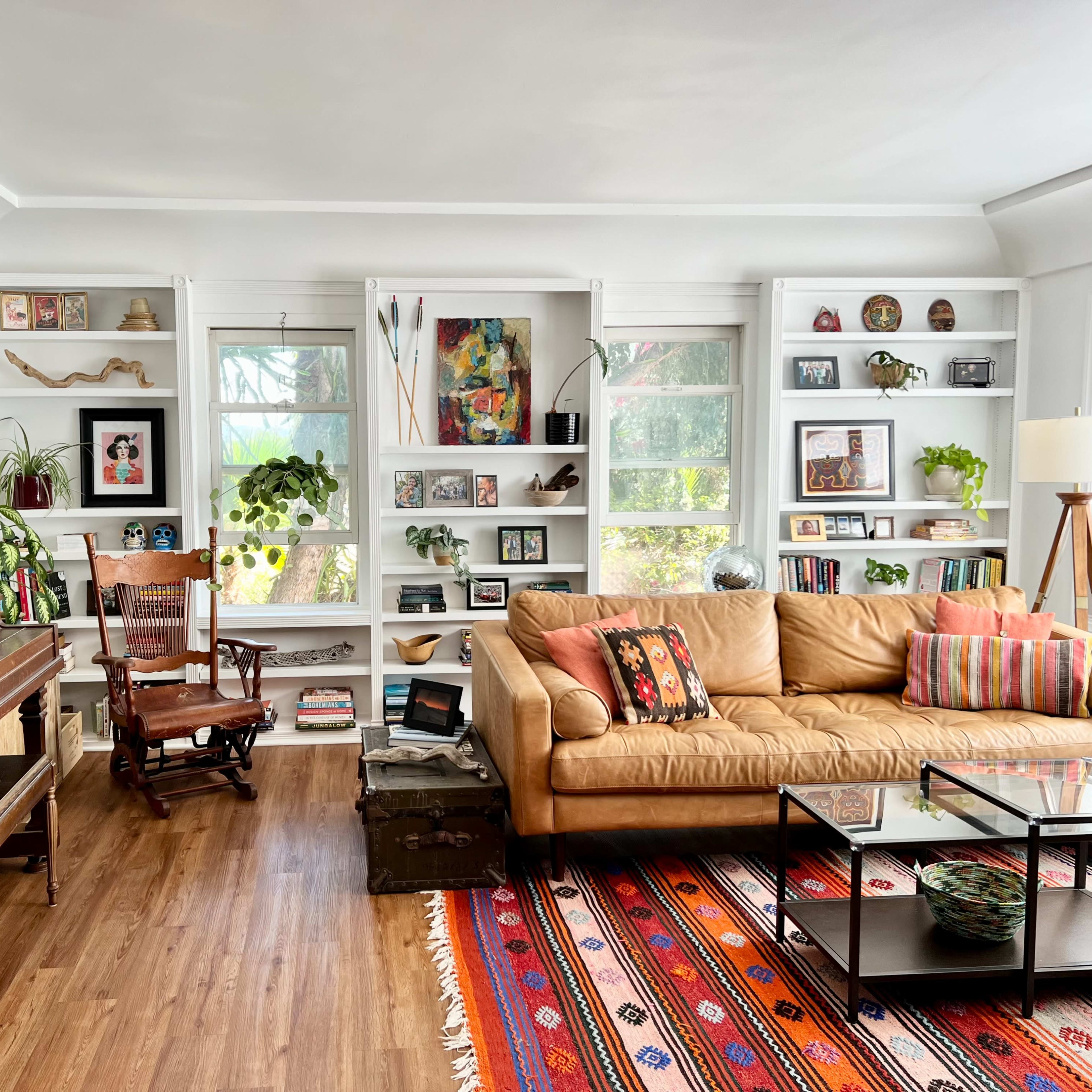 A cozy living room featuring a piano, an armchair, a beige couch with decorative pillows, and shelves filled with various decorations and plants.