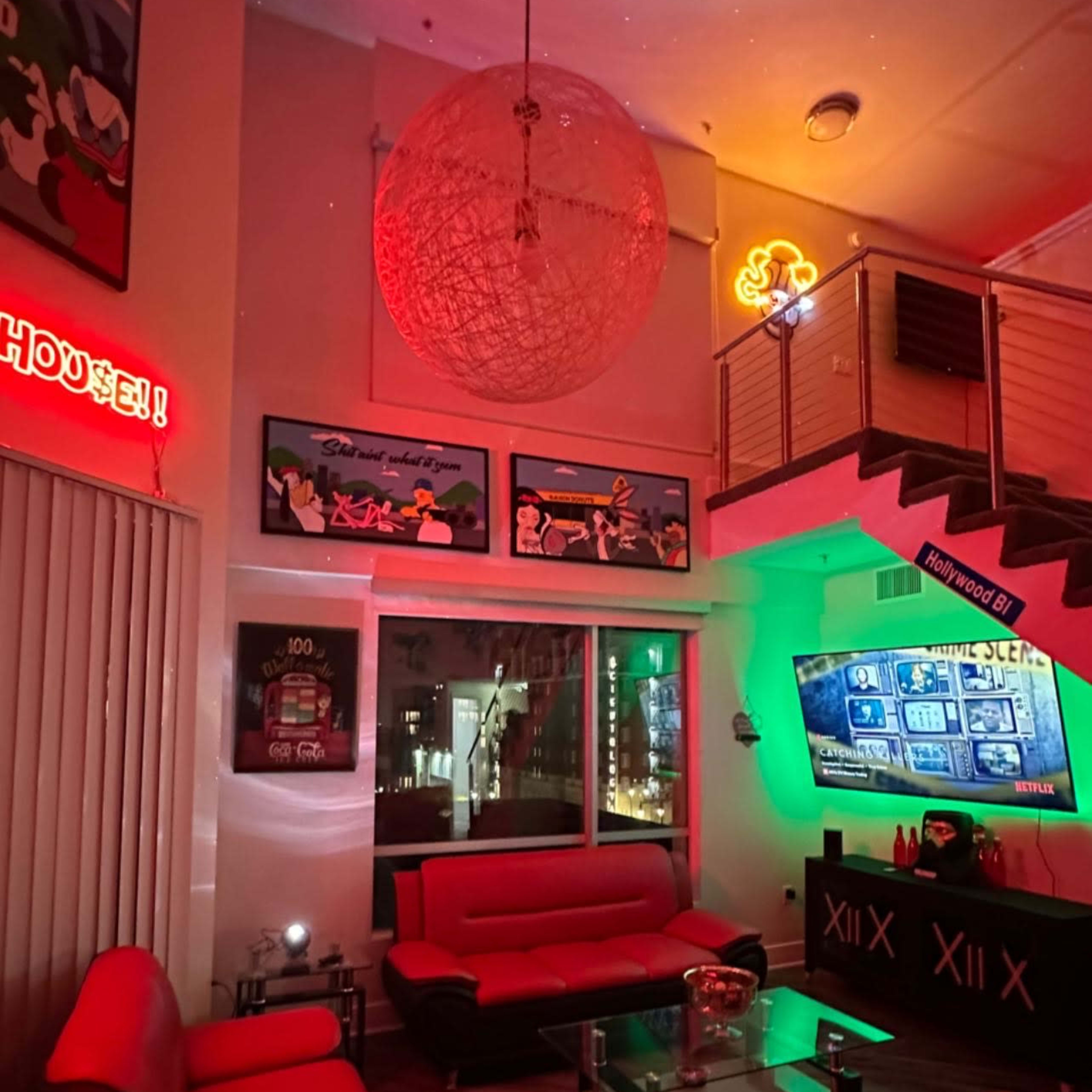 A modern lounge area with red seating, colorful lighting, and a large screen displaying a menu, alongside a sign offering rental and catering services.