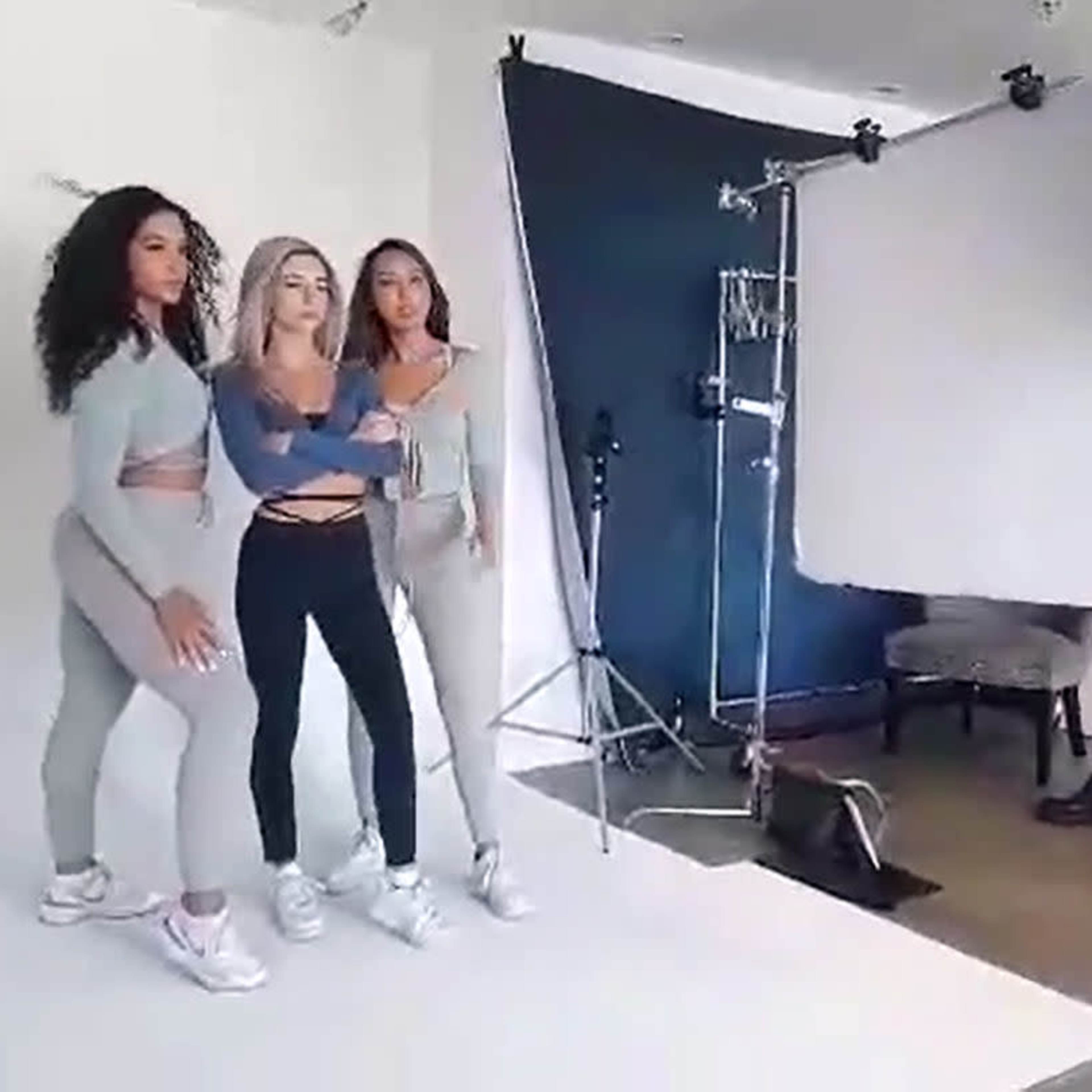 Three women pose together in a studio setting, with a photography light and backdrop set up behind them.