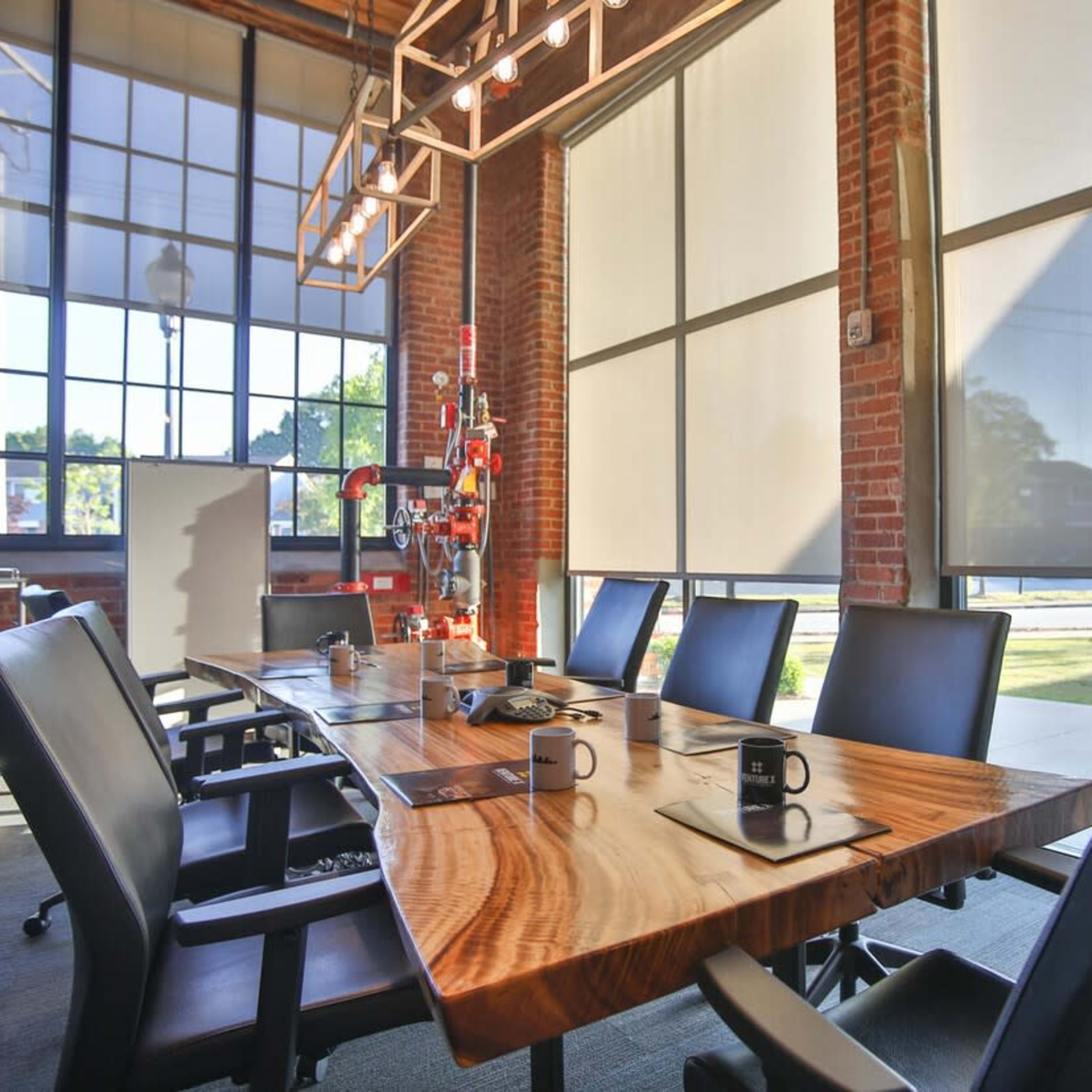 A conference room features a large wooden table surrounded by black chairs, with large windows letting in natural light.