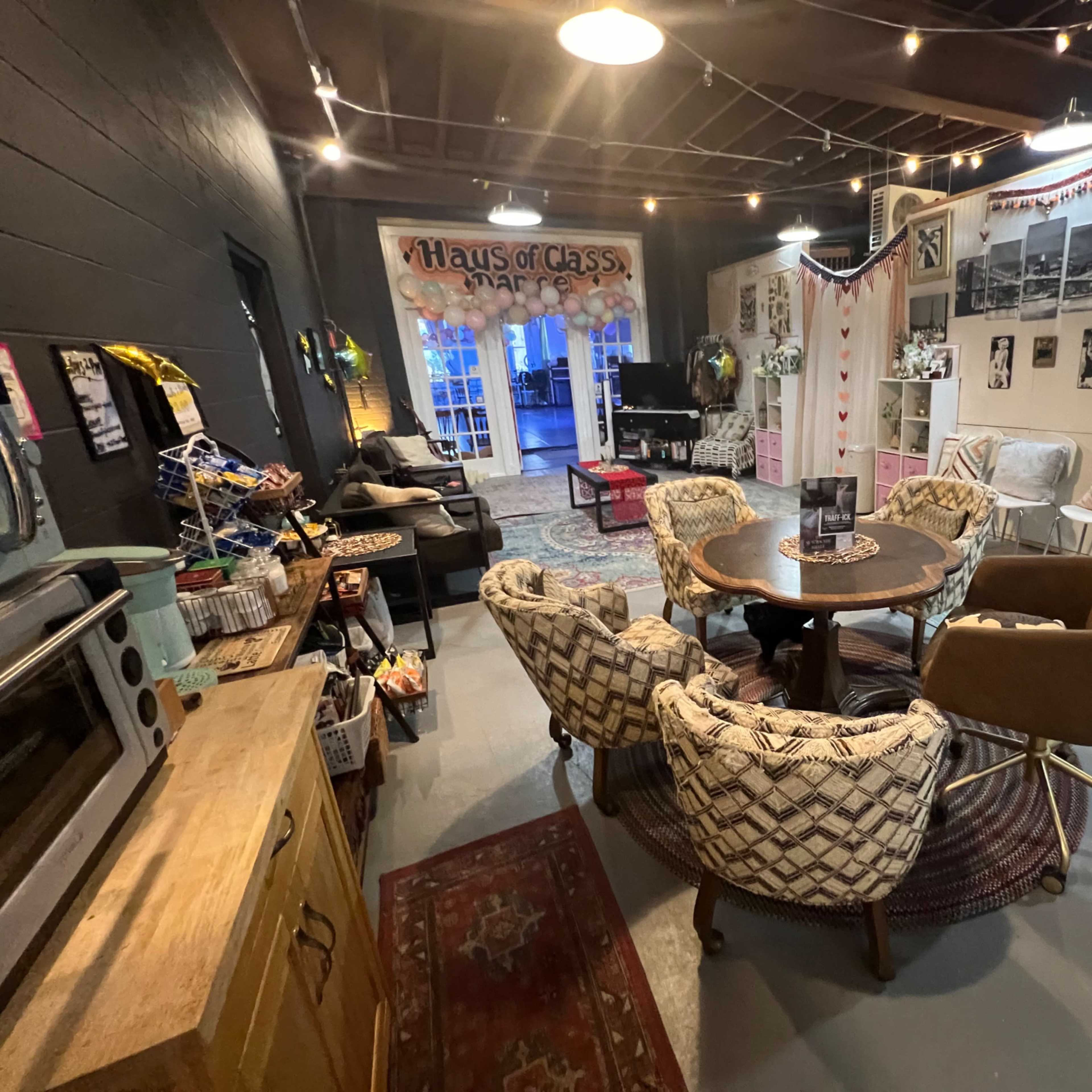 A cozy, multi-purpose room with a circular seating arrangement around a central table, decorated with rugs and wall art.