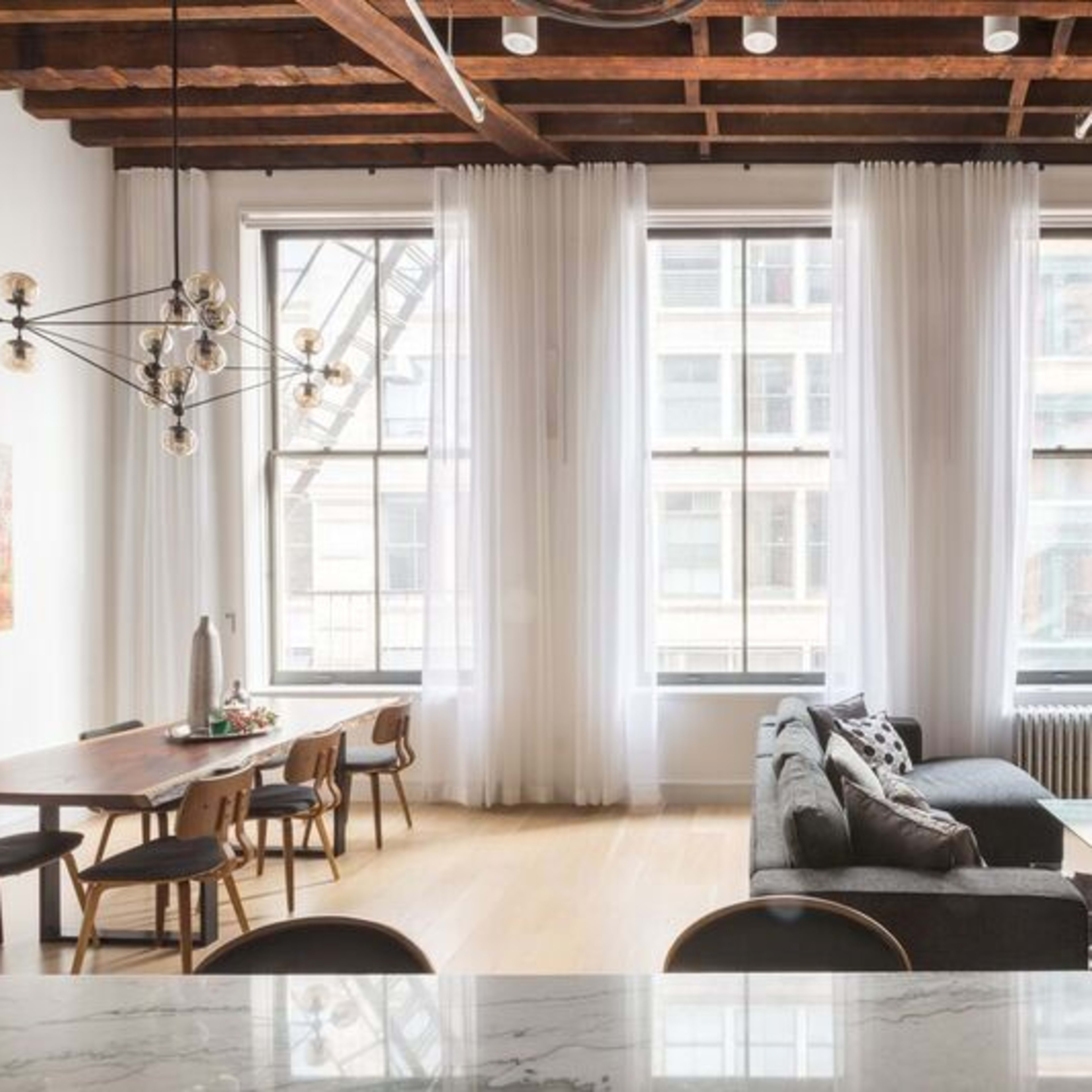 A modern, open-concept living space with large windows, a dining area with a wooden table, and a couch facing a wall-mounted television.
