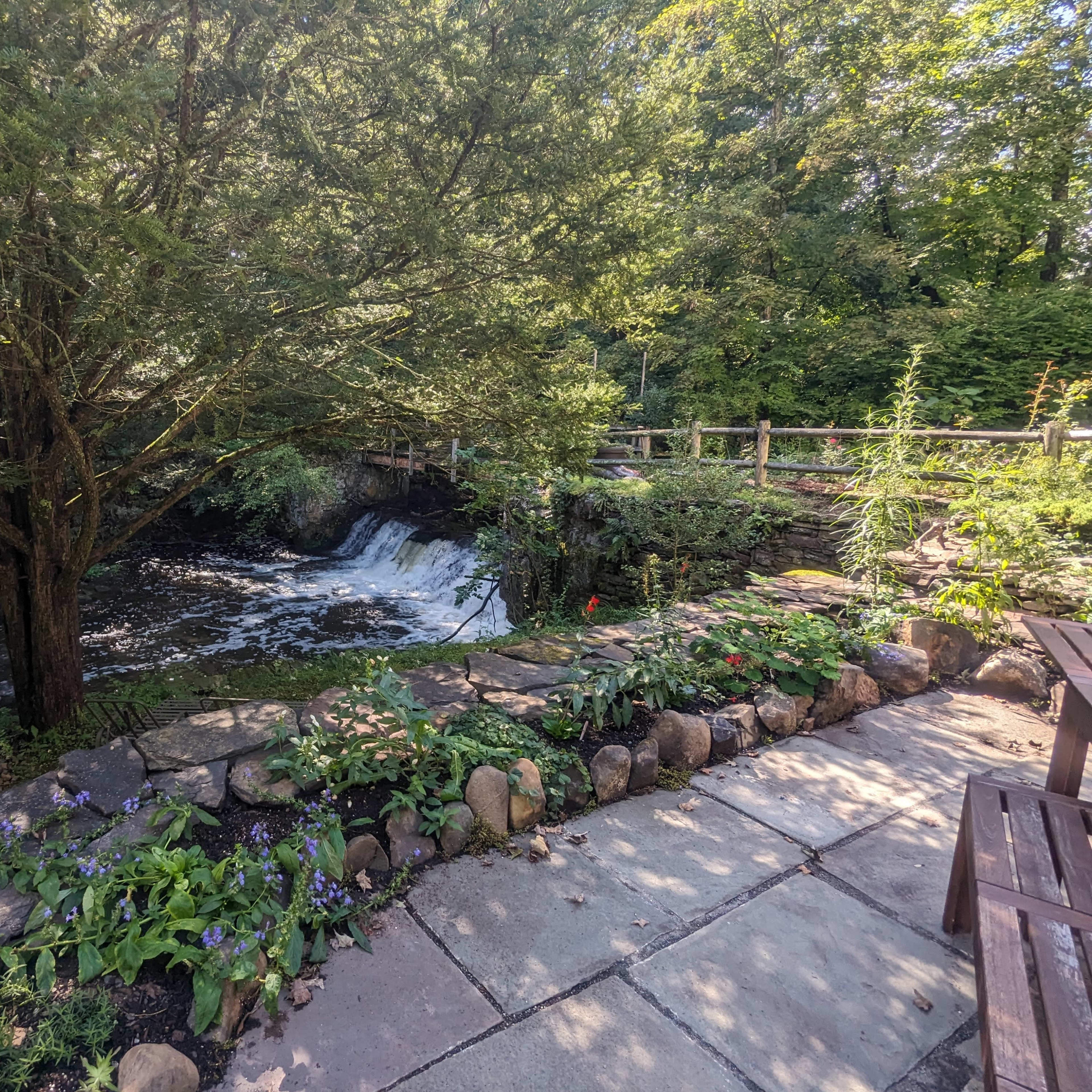 A stone-lined patio overlooks a cascading waterfall surrounded by lush greenery.