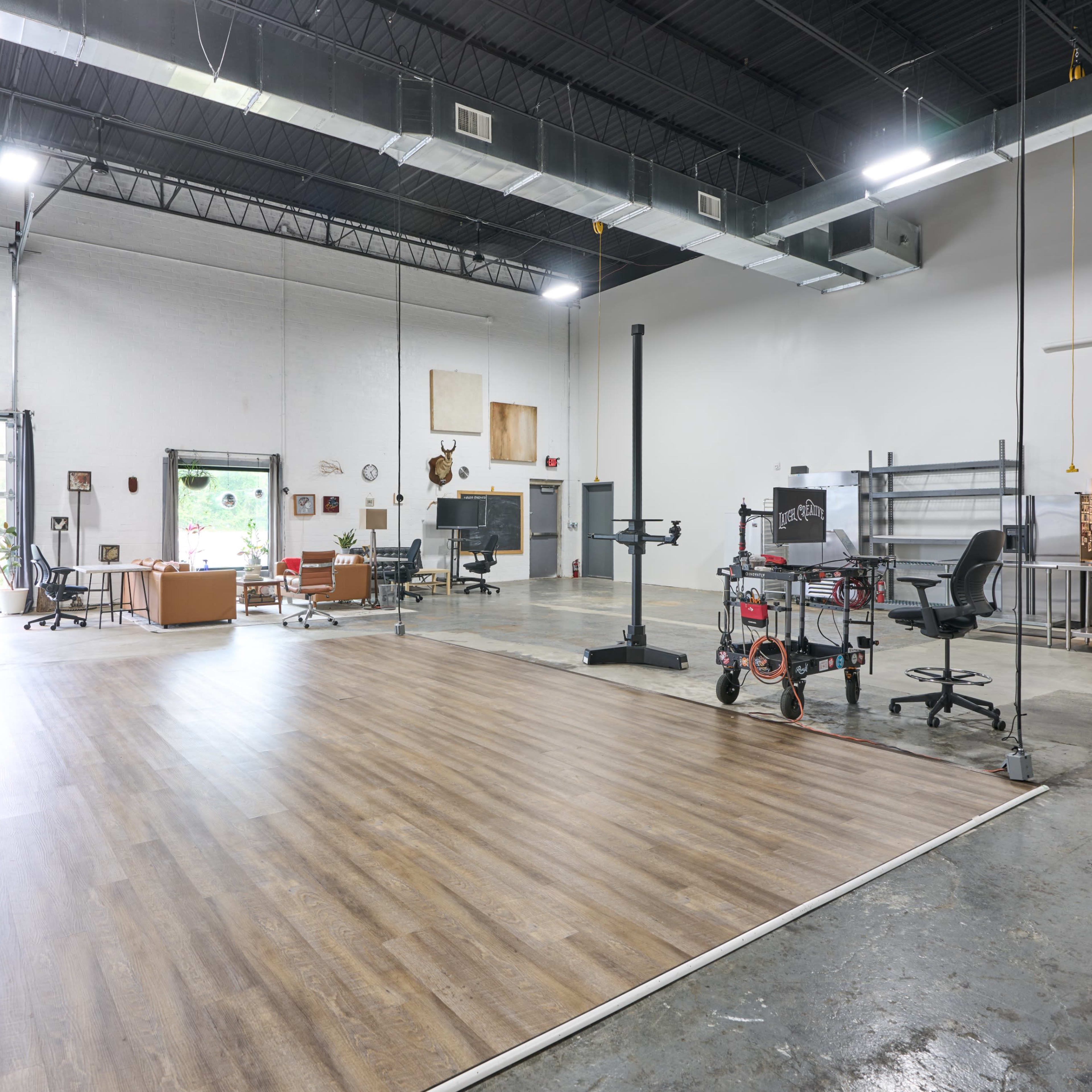 The spacious interior of a modern studio features hardwood flooring, industrial-style fixtures, and areas for seating, workstations, and a kitchenette.