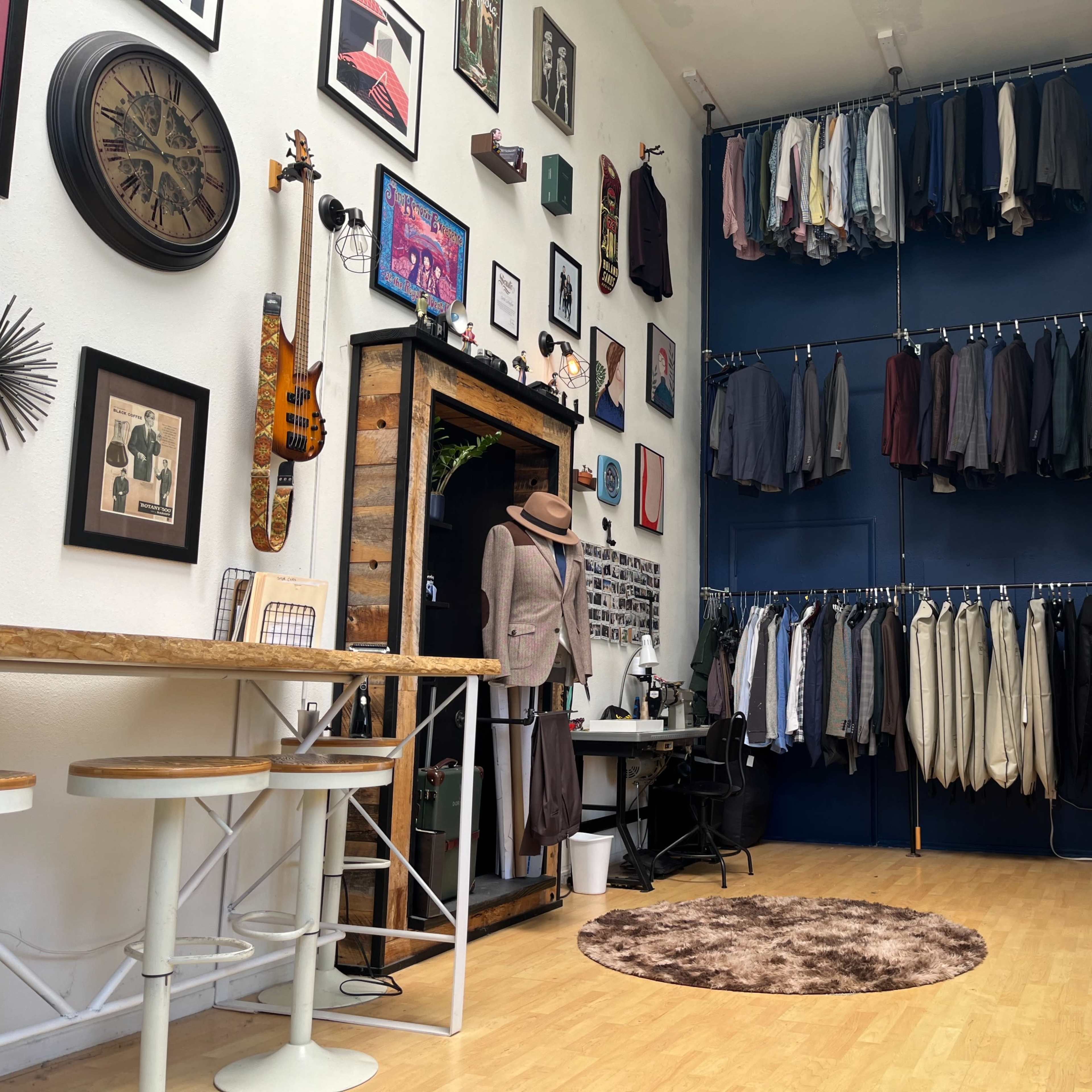 A stylish room with a display of framed art on the walls, hanging clothing organized on racks, and a seating area featuring a small table and chairs.