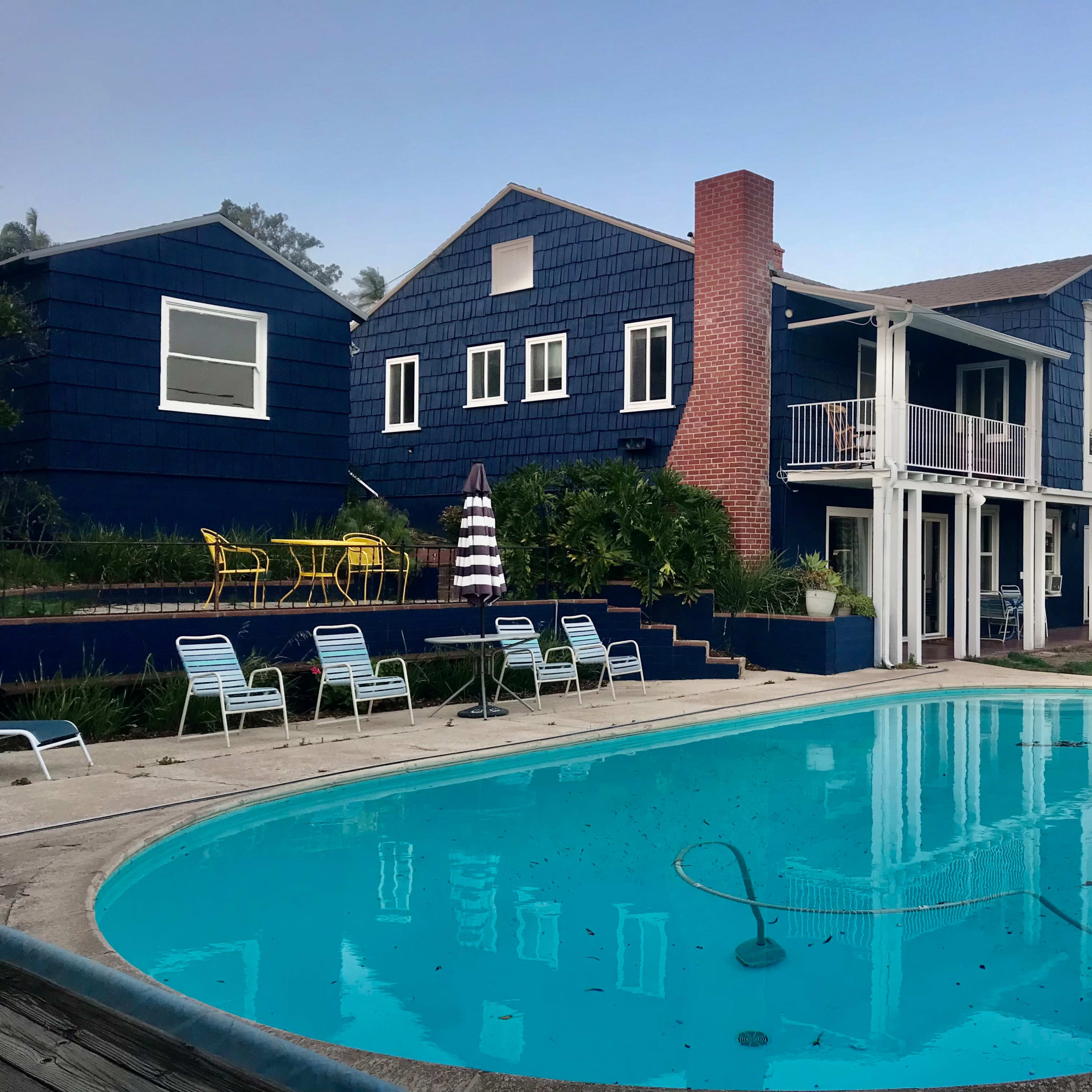 A rectangular pool reflects a blue two-story house with a chimney and outdoor seating.