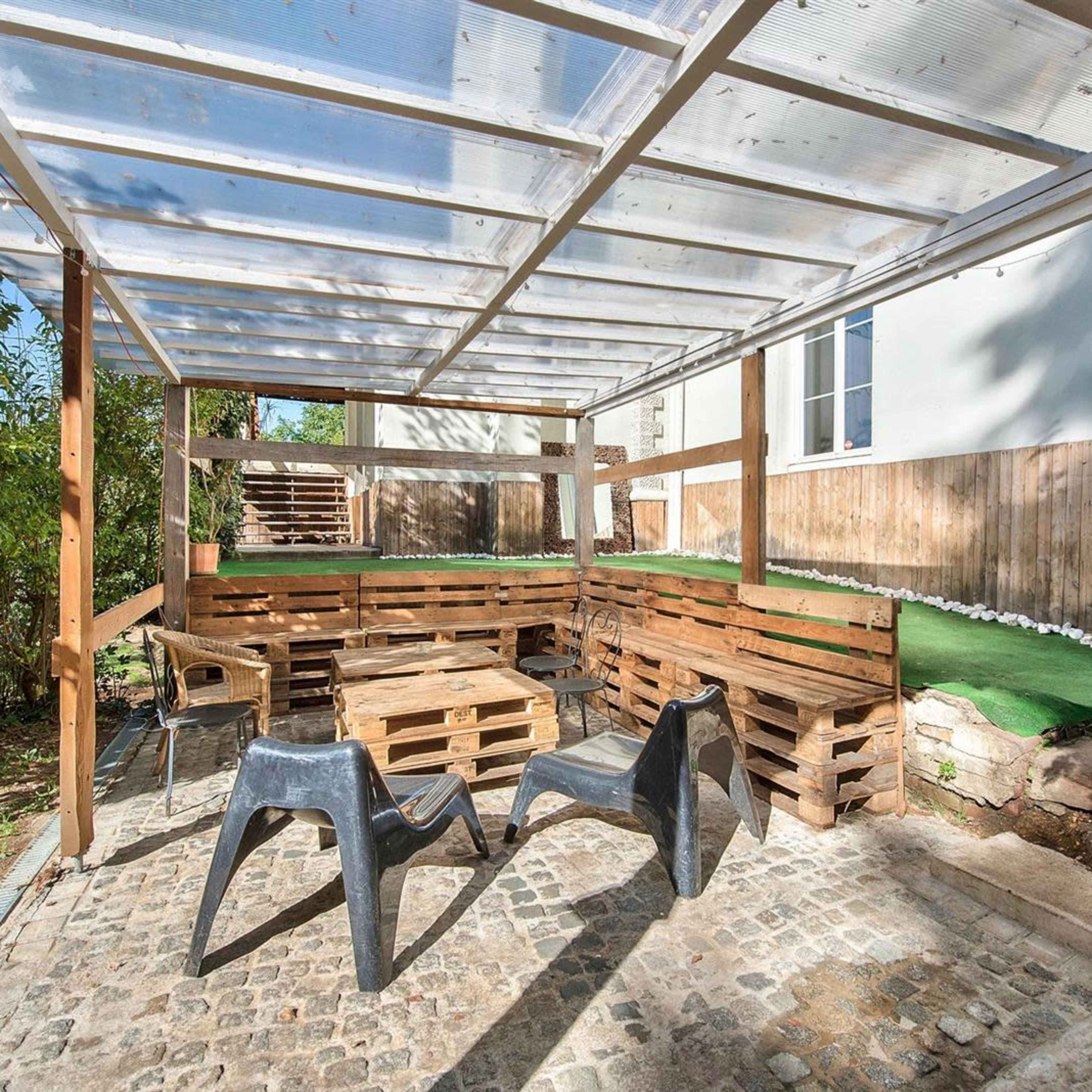 A covered outdoor seating area constructed with wooden pallets and featuring a stone pavement.