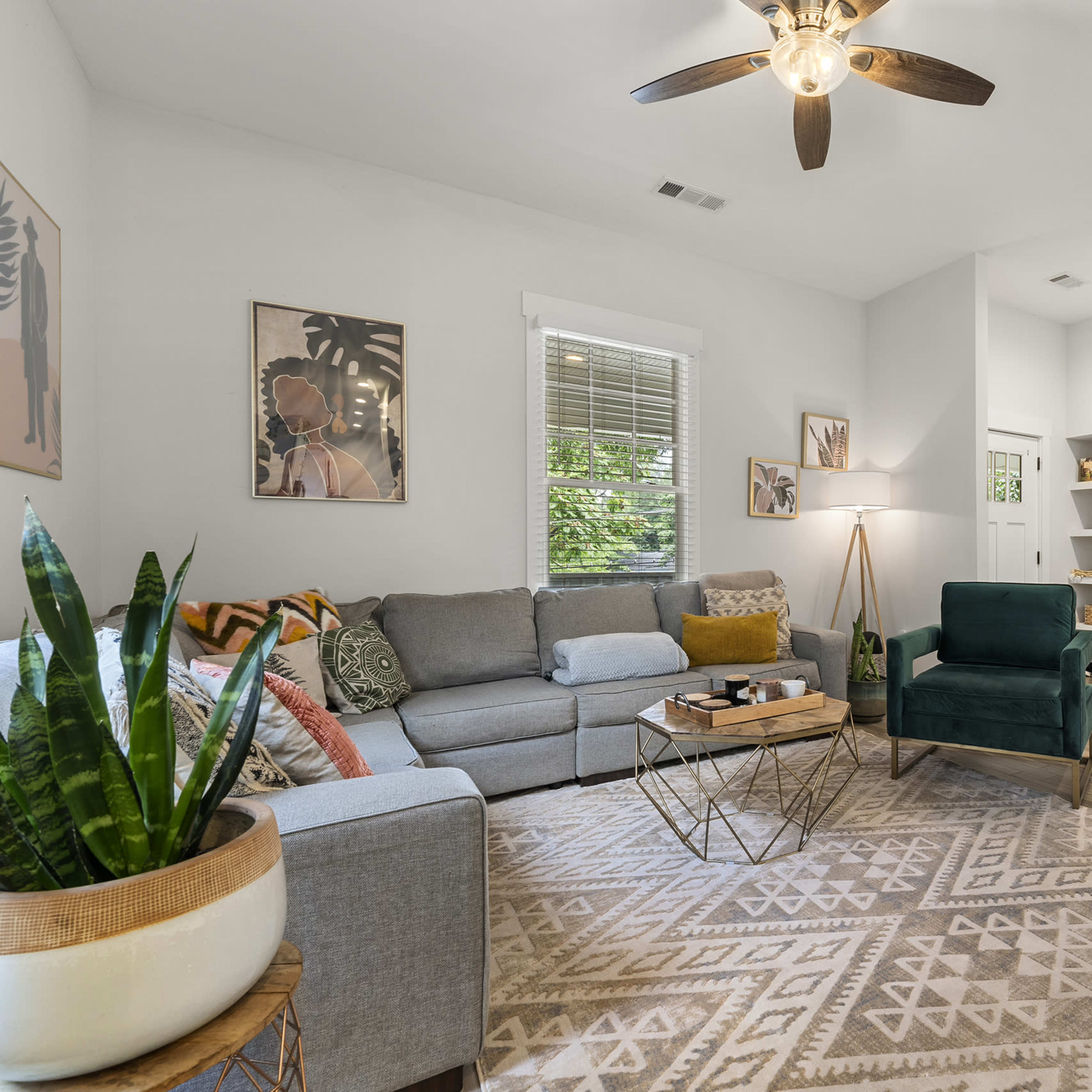 A cozy living room features a gray sectional sofa, a green armchair, a large area rug, and decorative wall art.