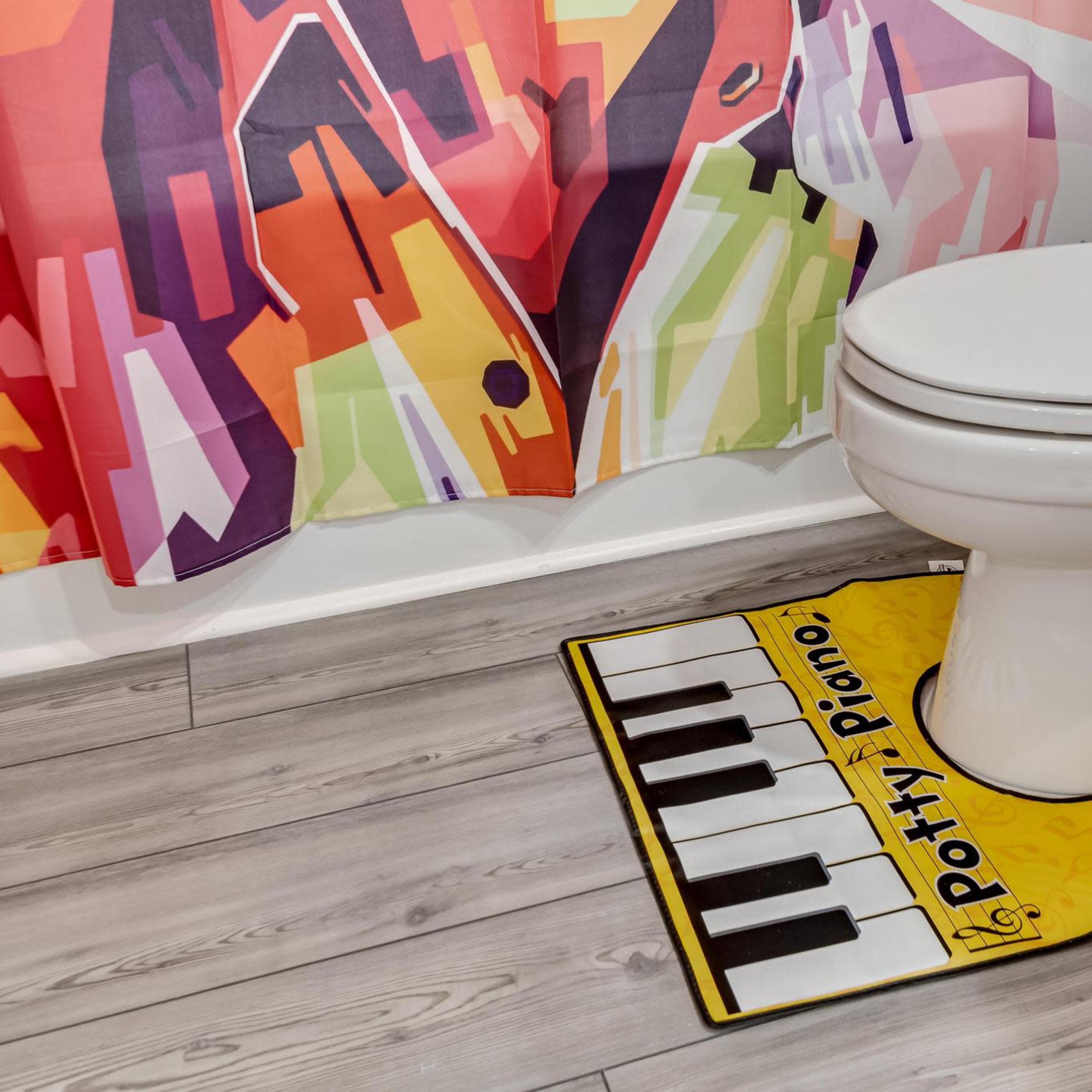 A colorful shower curtain hangs beside a toilet, with a novelty piano-themed bath mat placed on the floor.