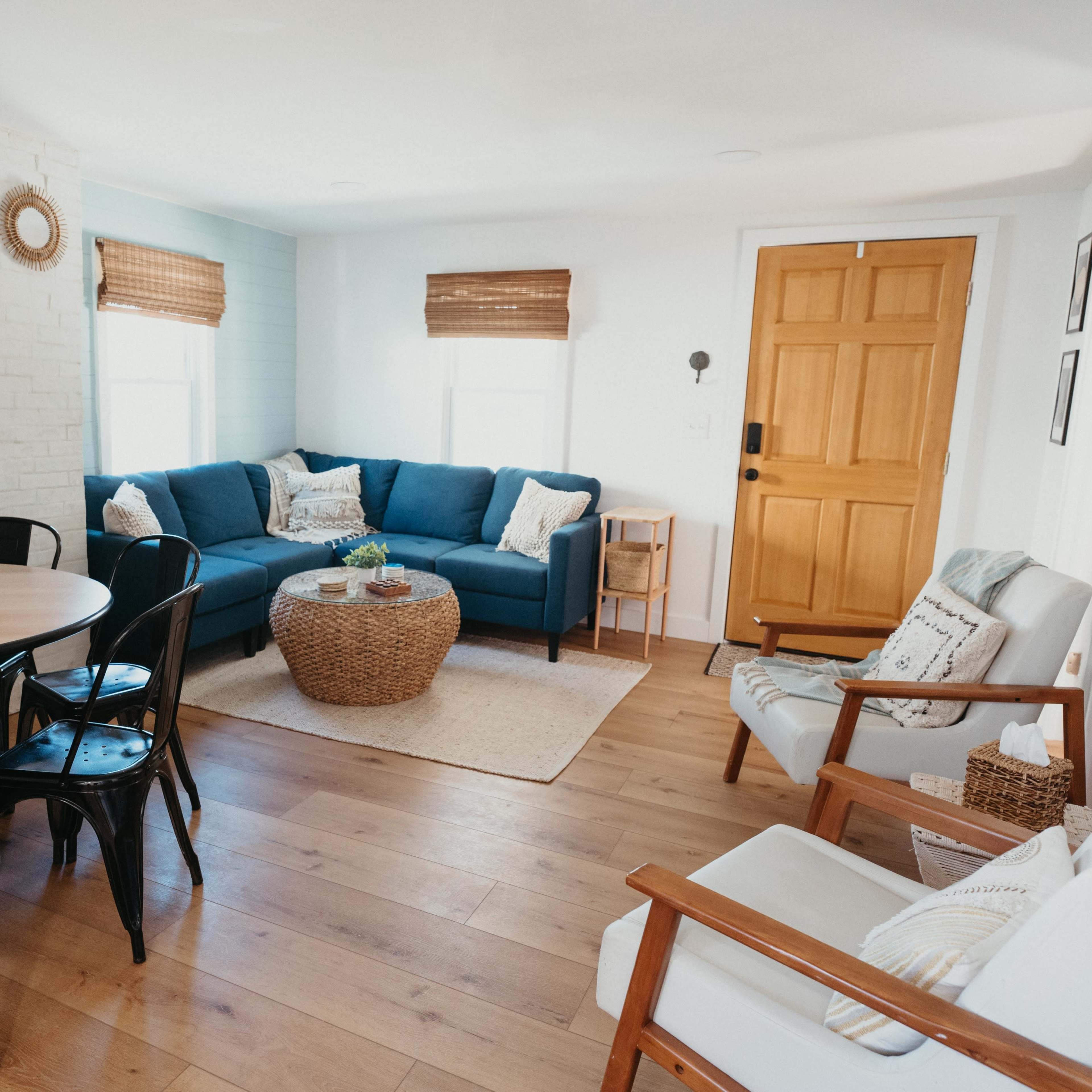 A bright, minimalist living room with a blue sofa, wooden table, and natural woven decor.