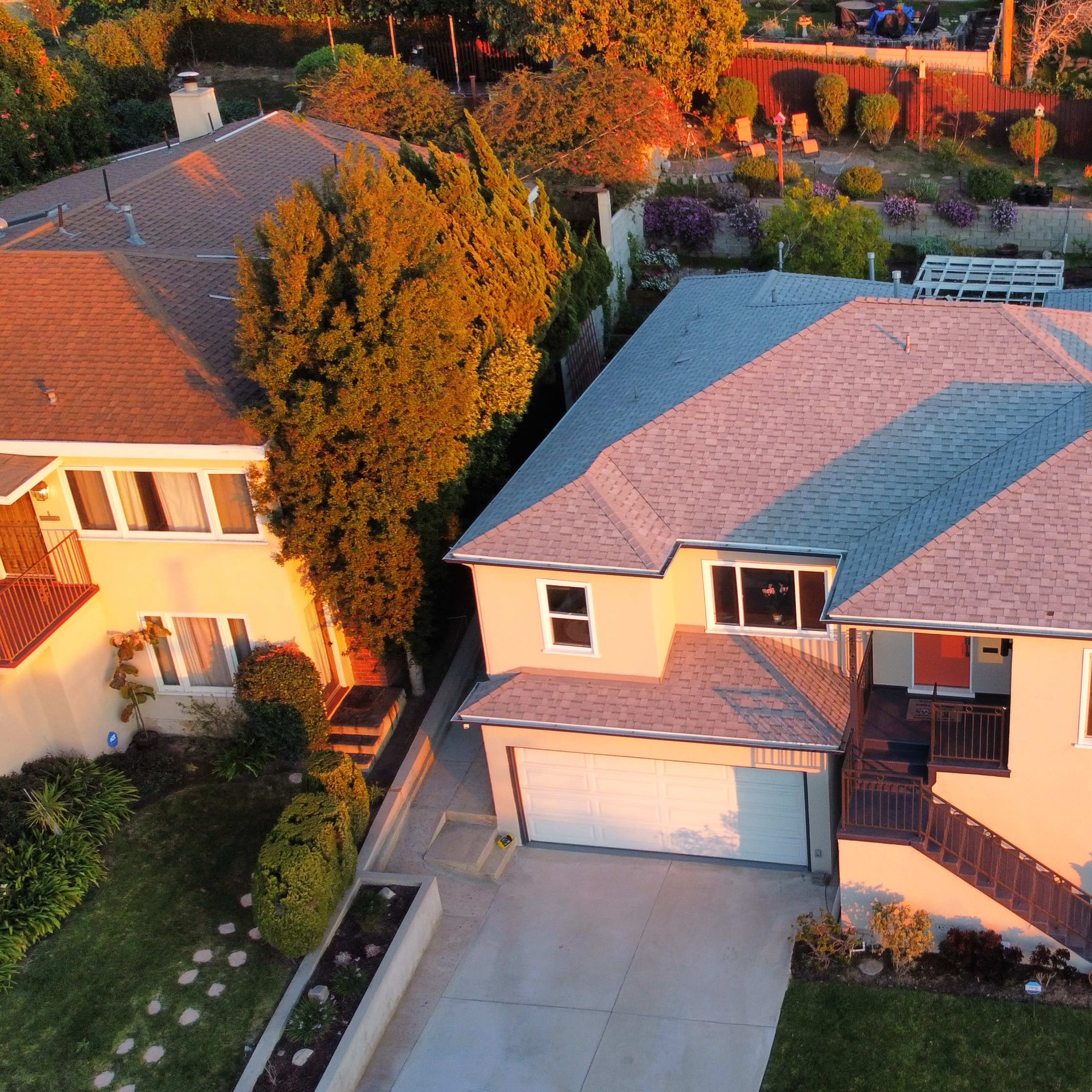 An aerial view shows a two-story house with a landscaped yard and a driveway, situated between two other homes in a suburban neighborhood.