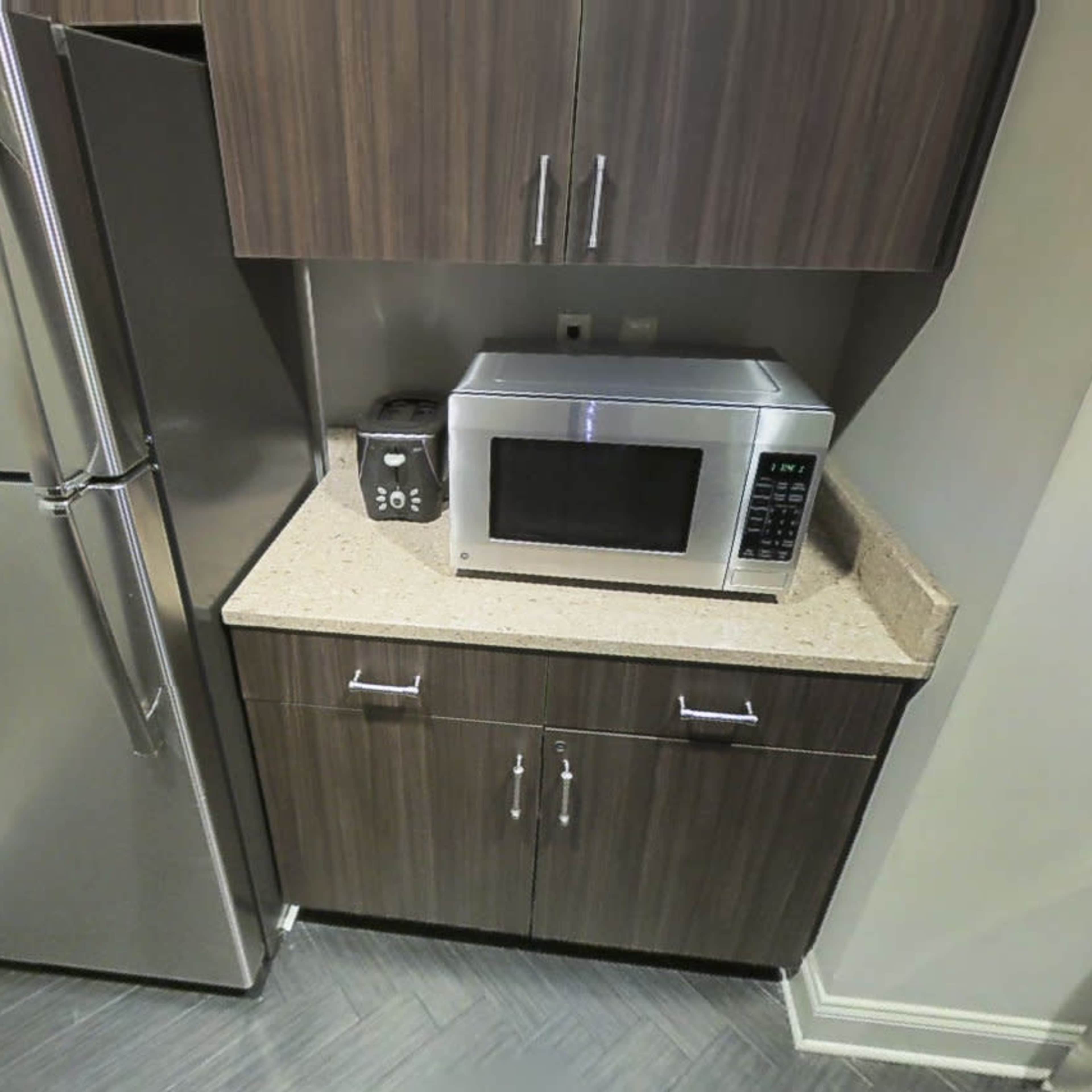 A kitchen corner with a stainless steel refrigerator next to a microwave on a countertop, below cabinets.