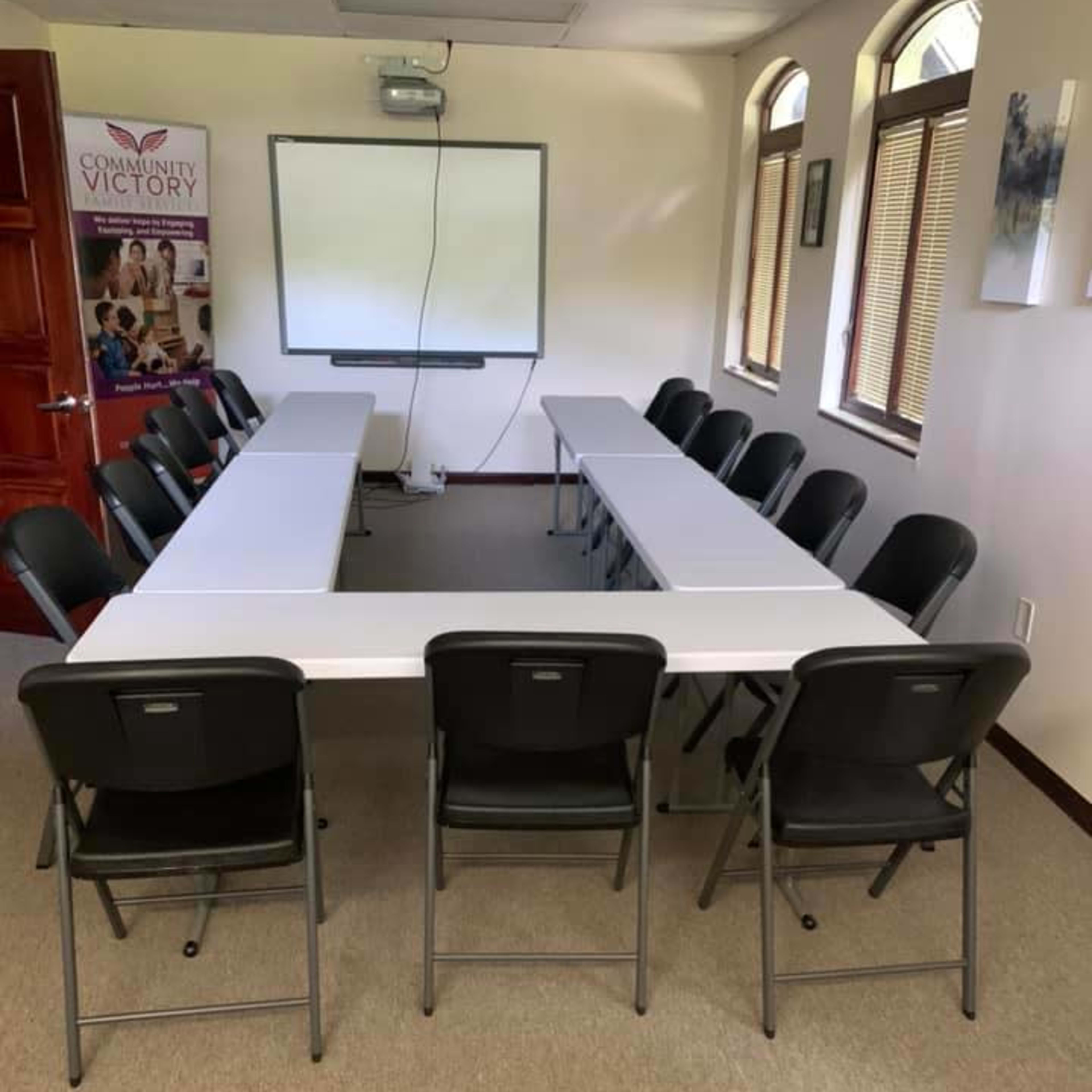 A rectangular conference room table surrounded by black folding chairs is set up in a well-lit meeting space.