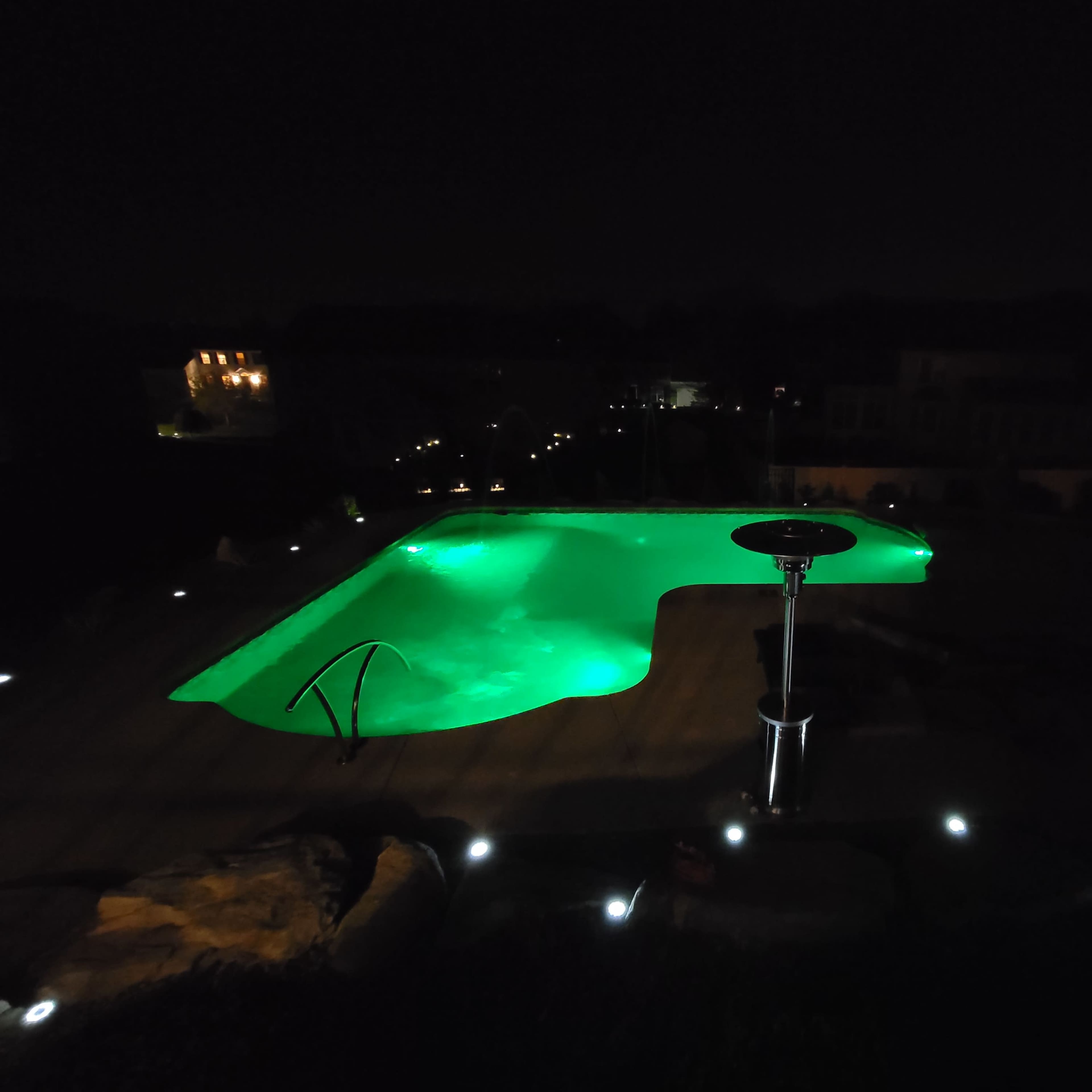 A pool illuminated with green lights is surrounded by dimly lit landscaping at night.