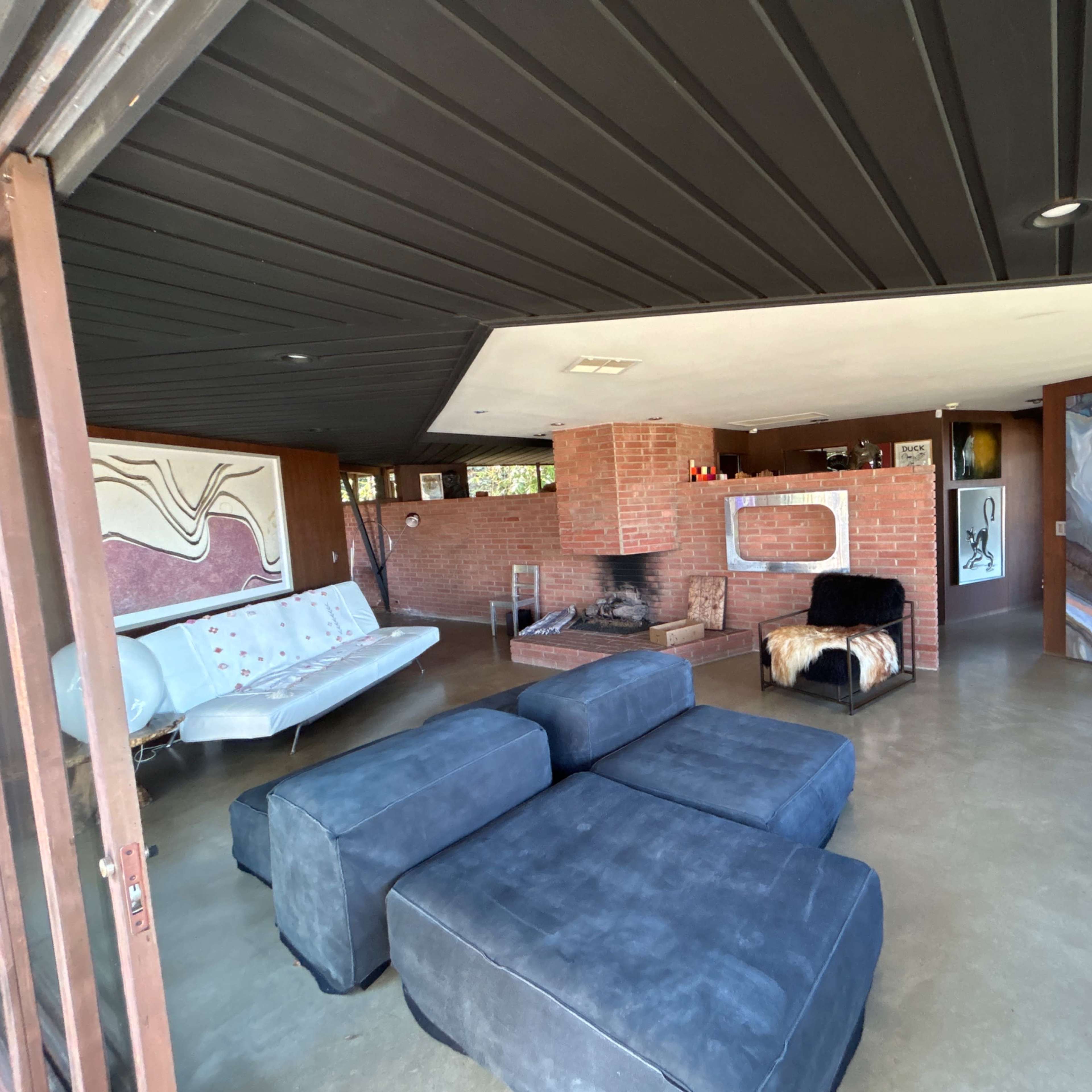 A modern living room with a mix of brick and concrete walls, featuring a sectional sofa, a fireplace, and large artwork on the walls.