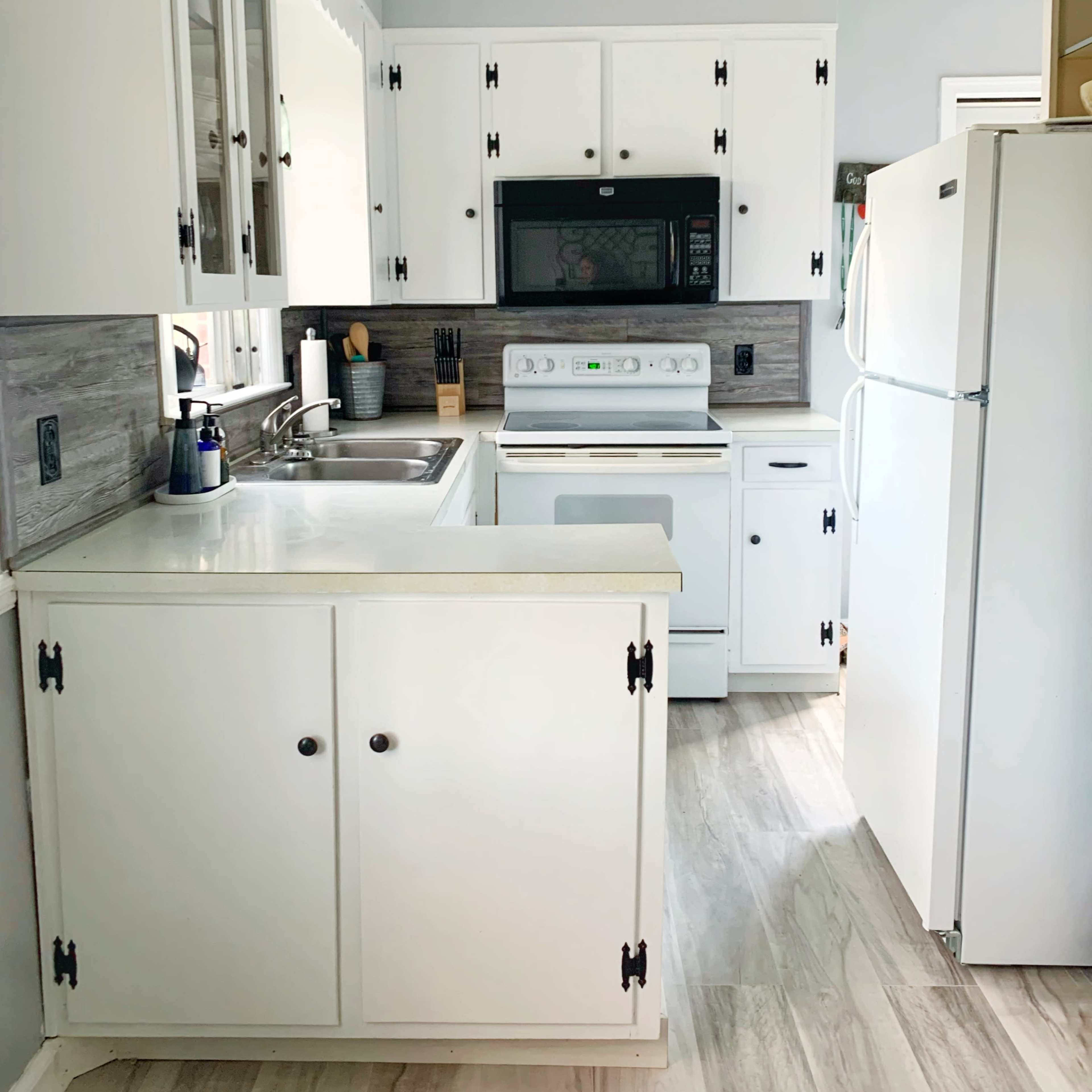 A small kitchen features white cabinets, a sink, a microwave, an oven, and a refrigerator.
