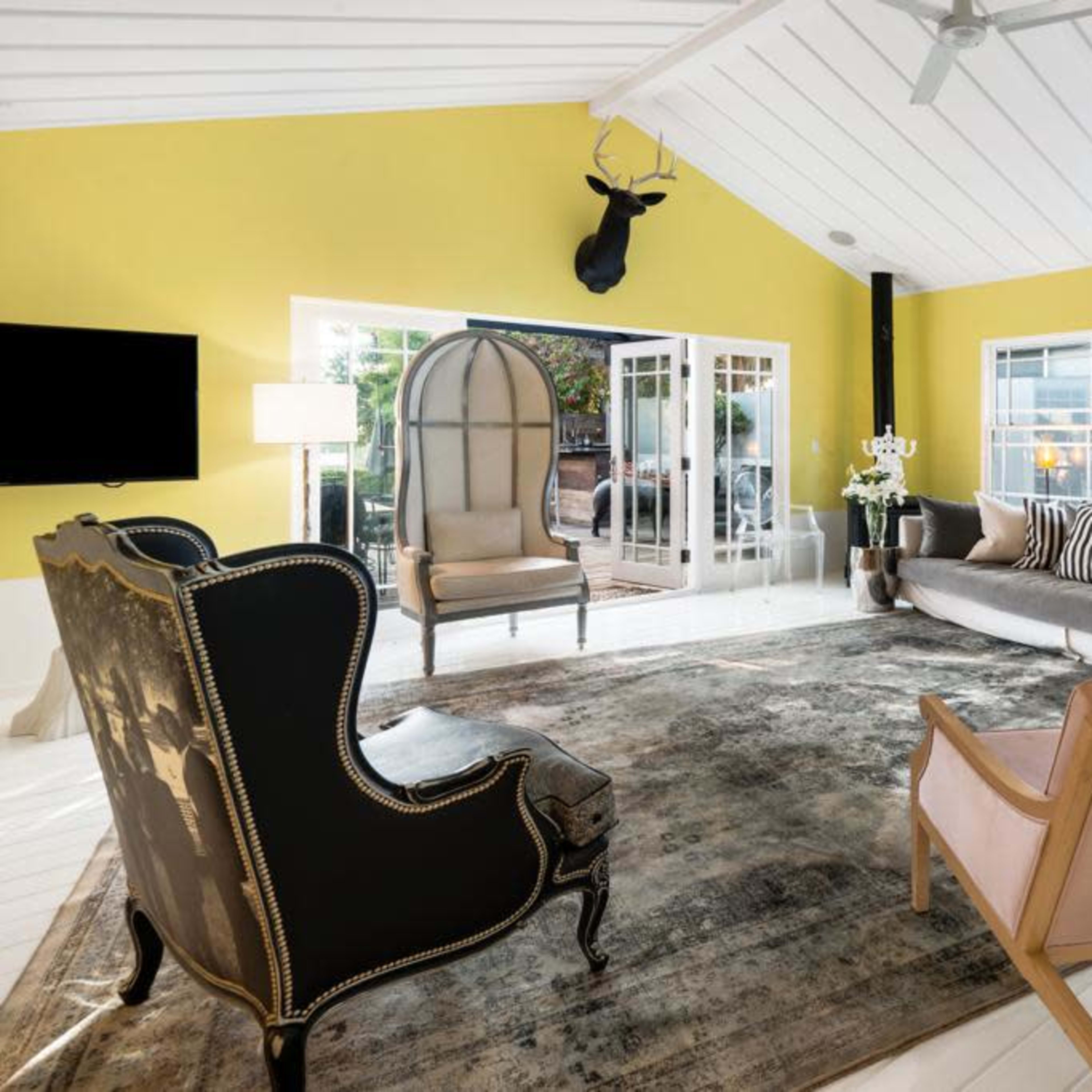 The room features a bright yellow wall, contemporary furniture, a large area rug, and large windows allowing natural light to fill the space.
