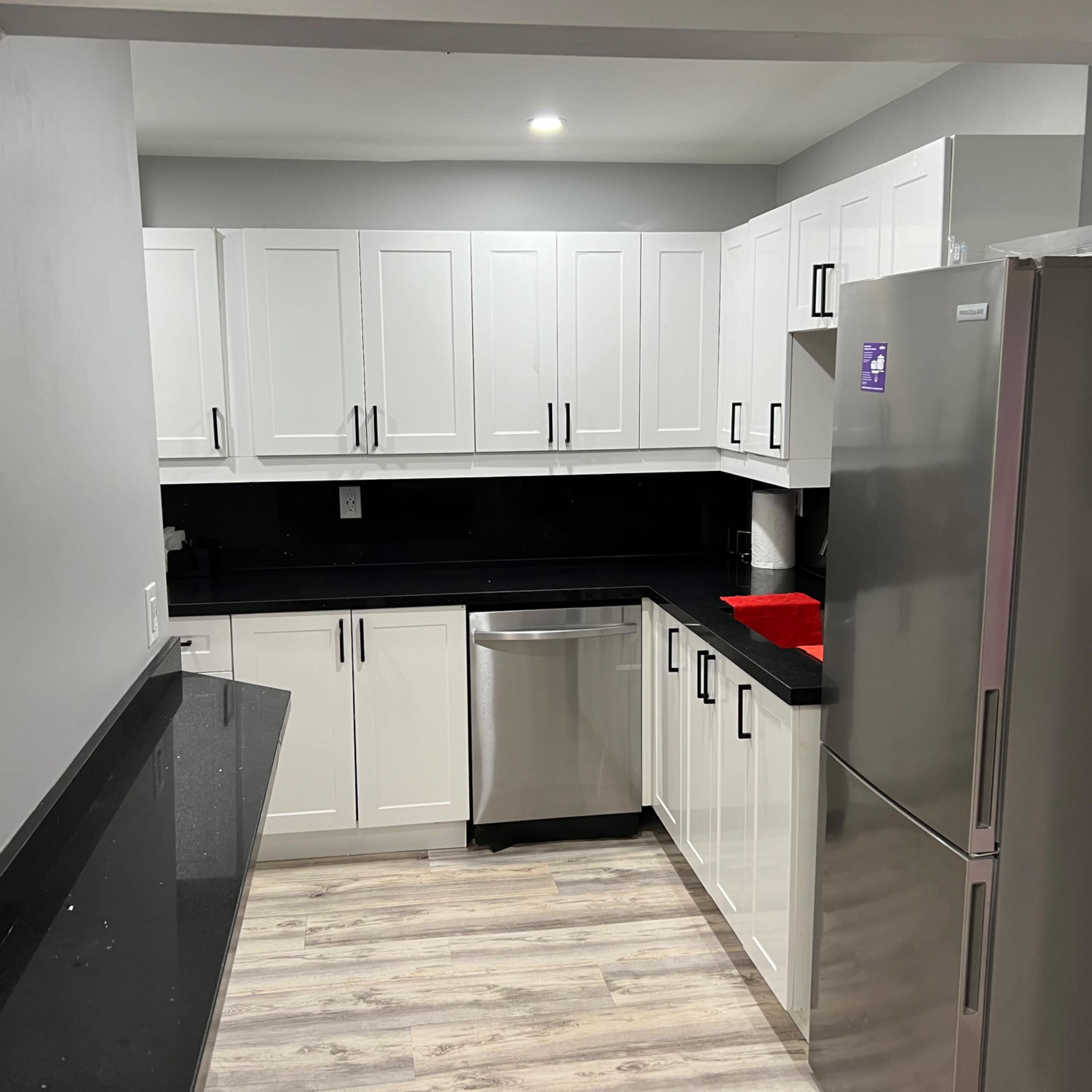A modern kitchen featuring white cabinetry, a stainless steel refrigerator, and black countertops.