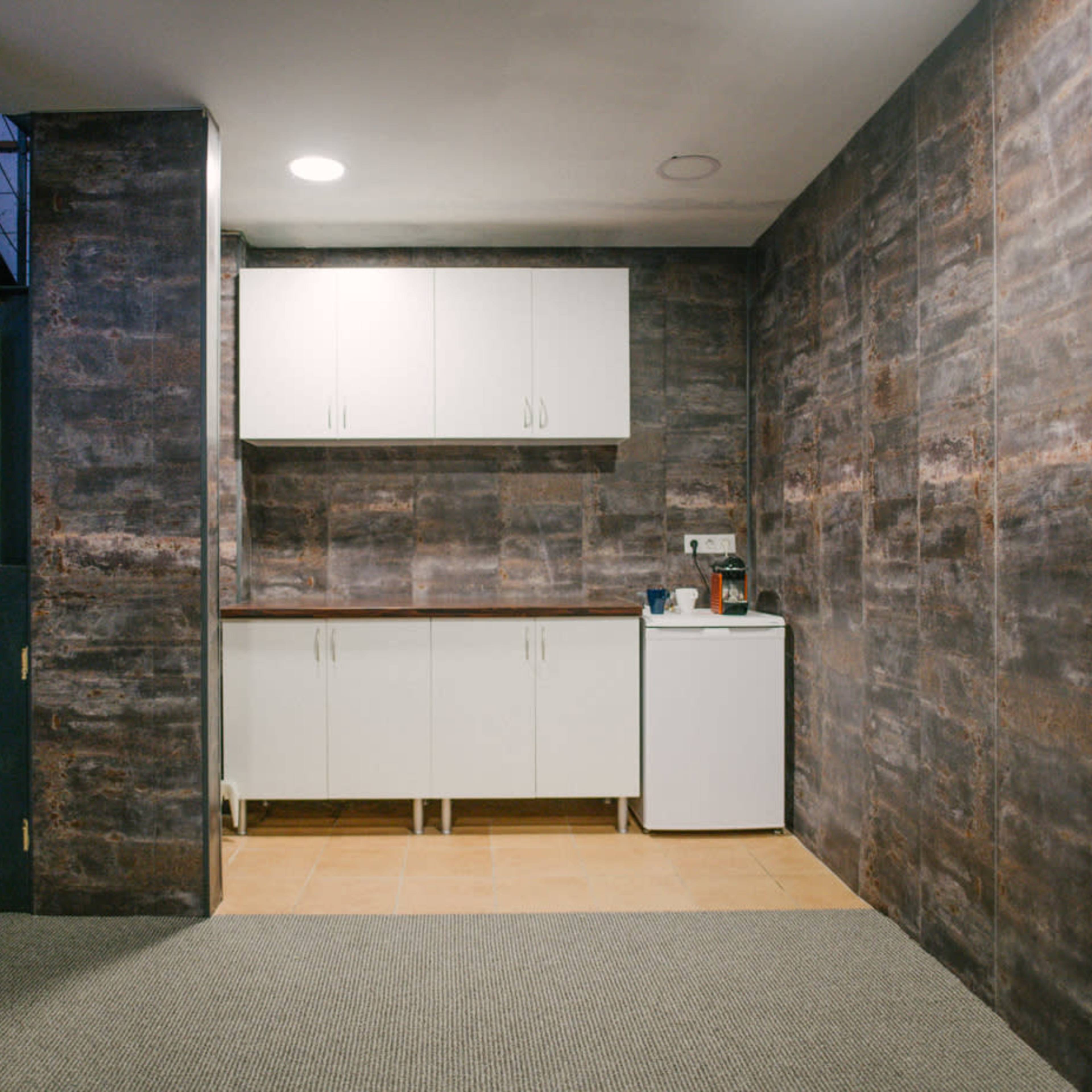 A kitchen area with white cabinets, a countertop, and a refrigerator against a textured stone wall.