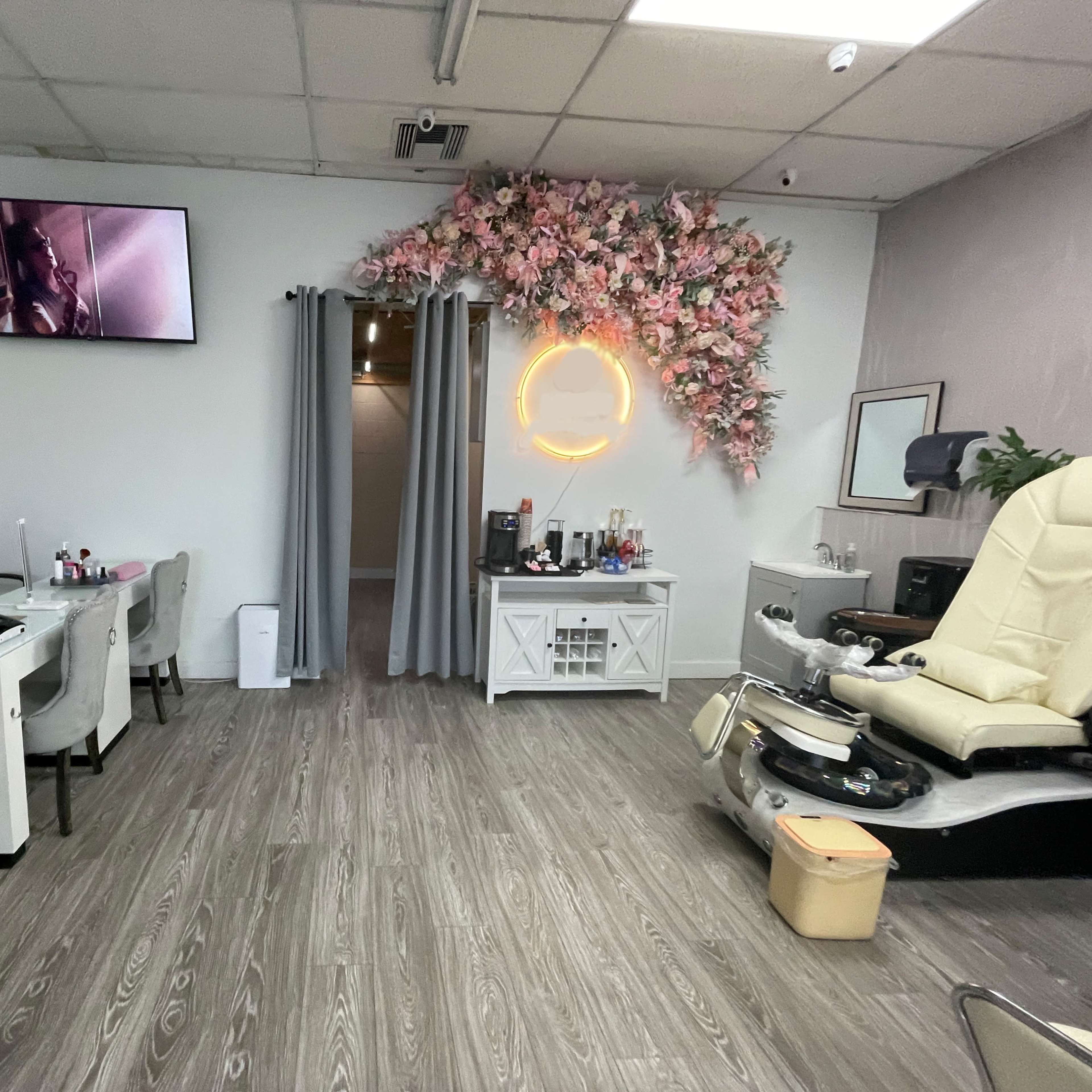 A nail salon with two workstations, a pedicure chair, a decorative floral wall, and a television mounted on the wall.