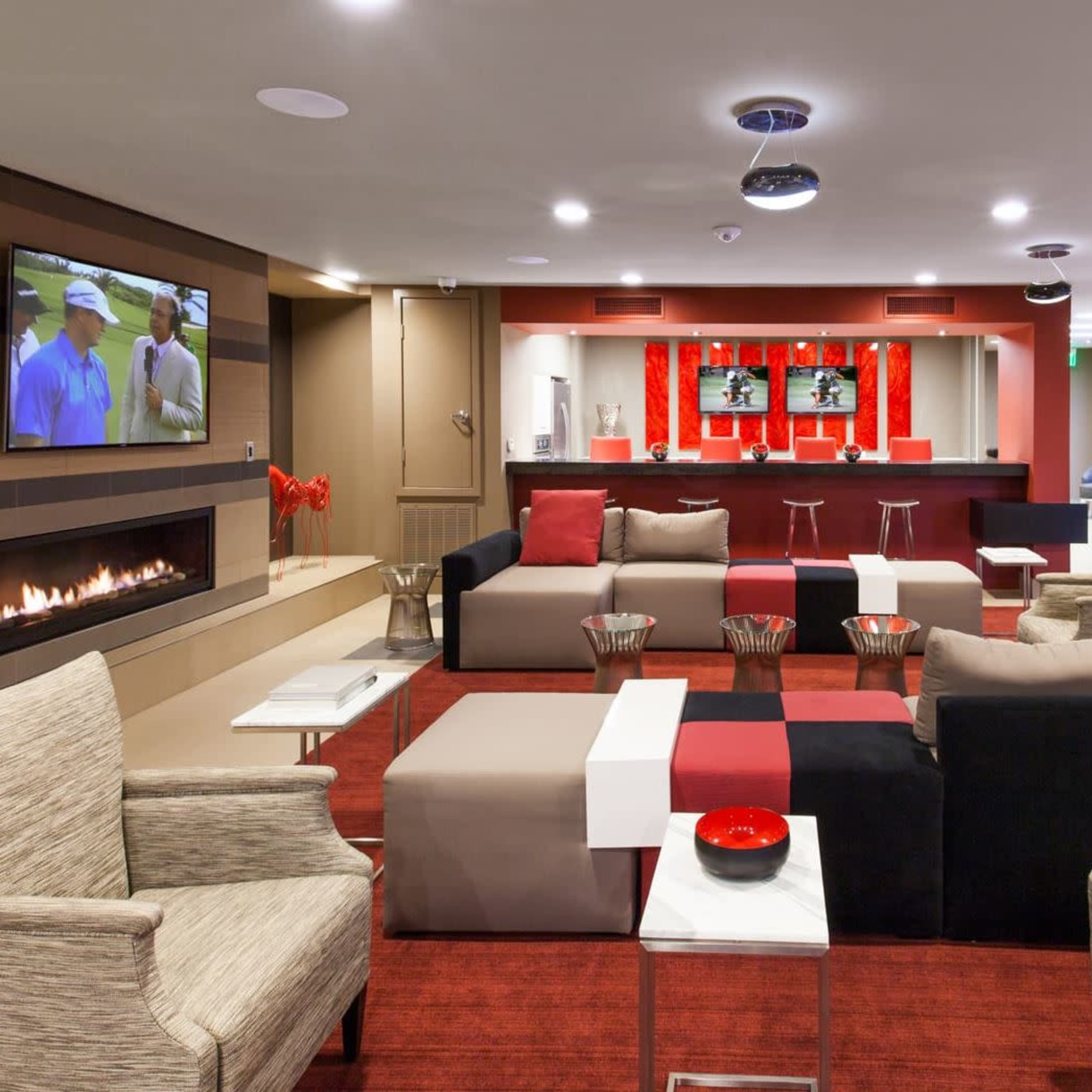 The modern lounge area features comfortable seating arrangements, a flat-screen TV, and a bar with high stools, all set against a backdrop of contemporary decor.