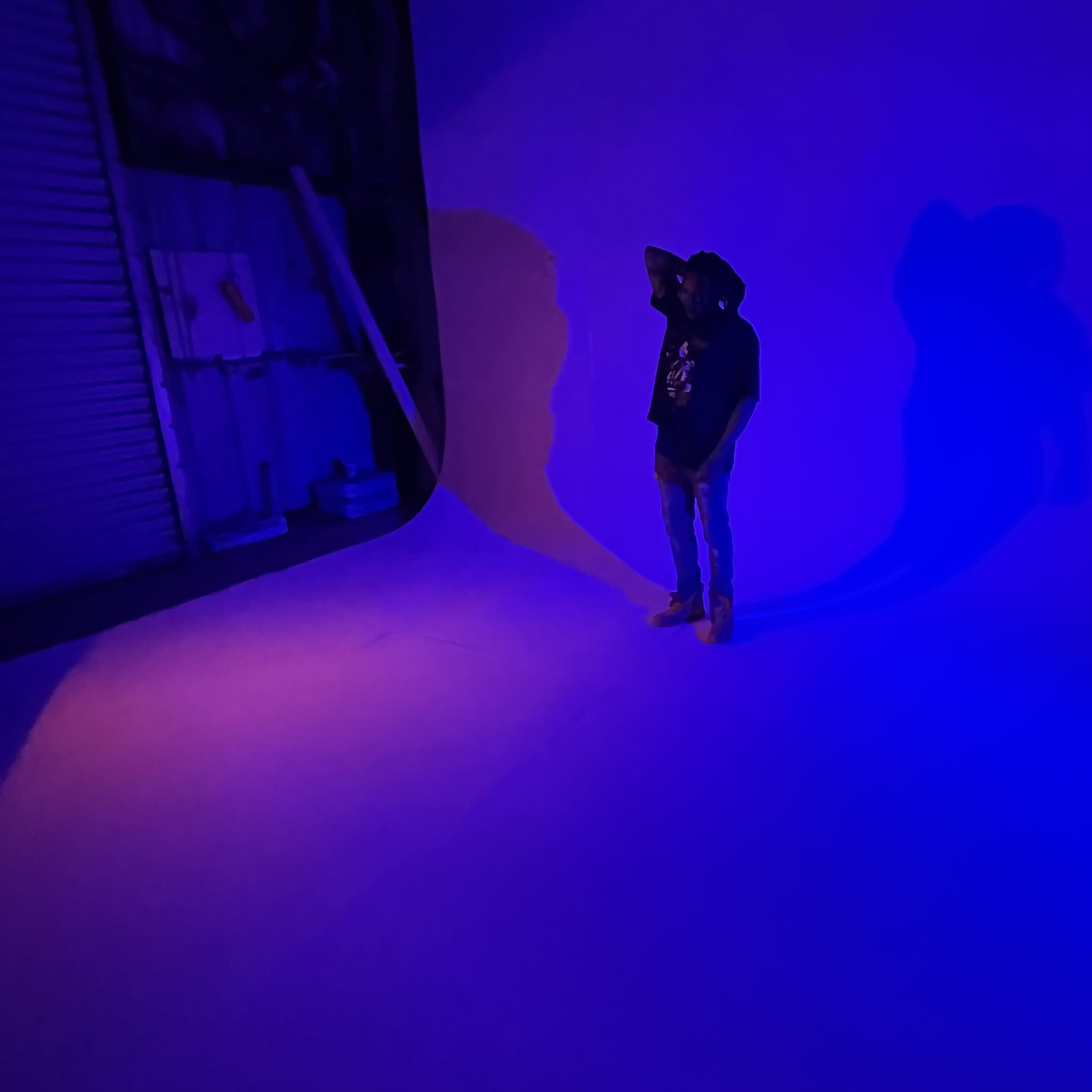 A person stands in front of a large curved backdrop illuminated with blue light, casting long shadows on the floor.