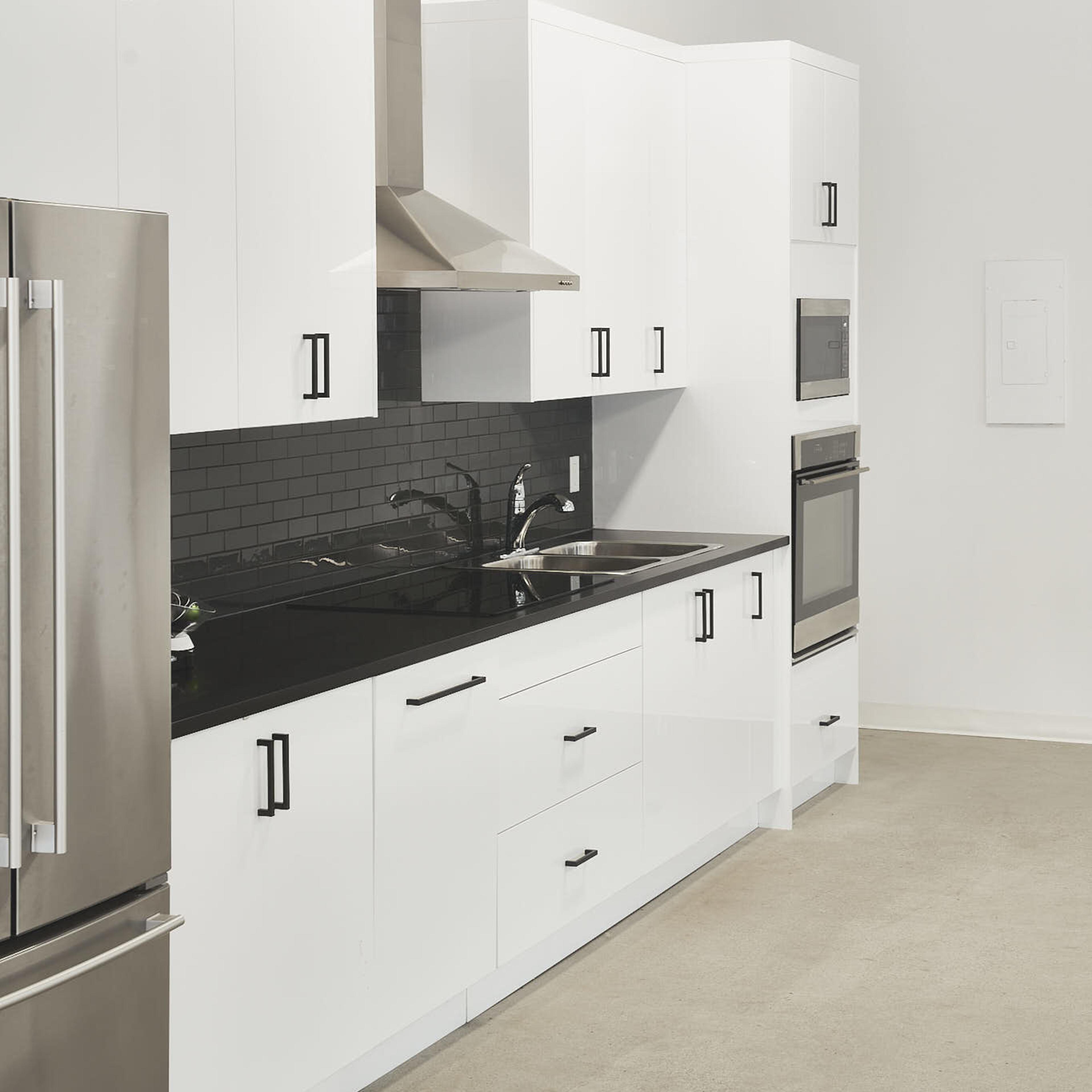 A modern kitchen with white cabinets, stainless steel appliances, and a black backsplash.