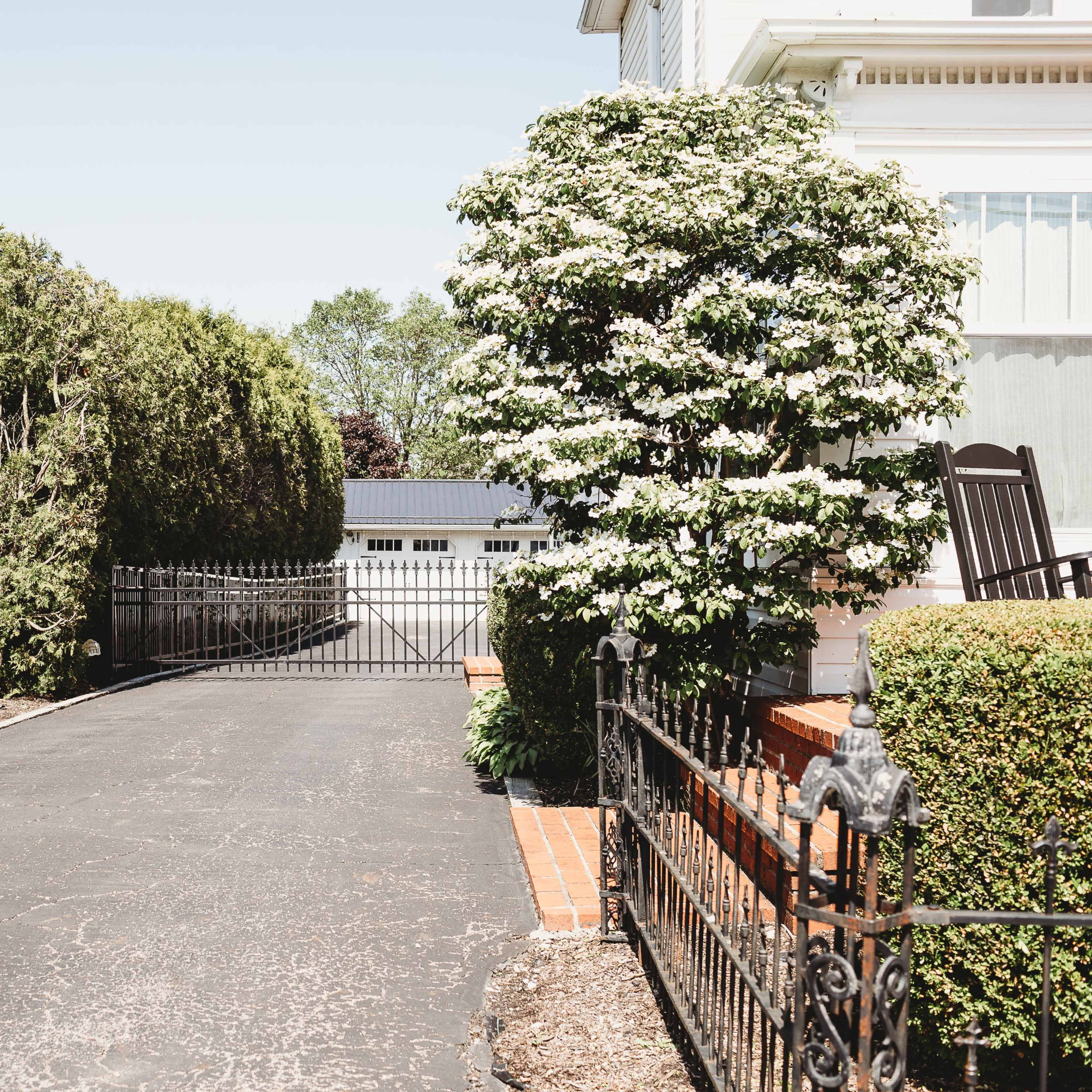 A paved driveway leads to a gated entrance with a fenced garden on either side.