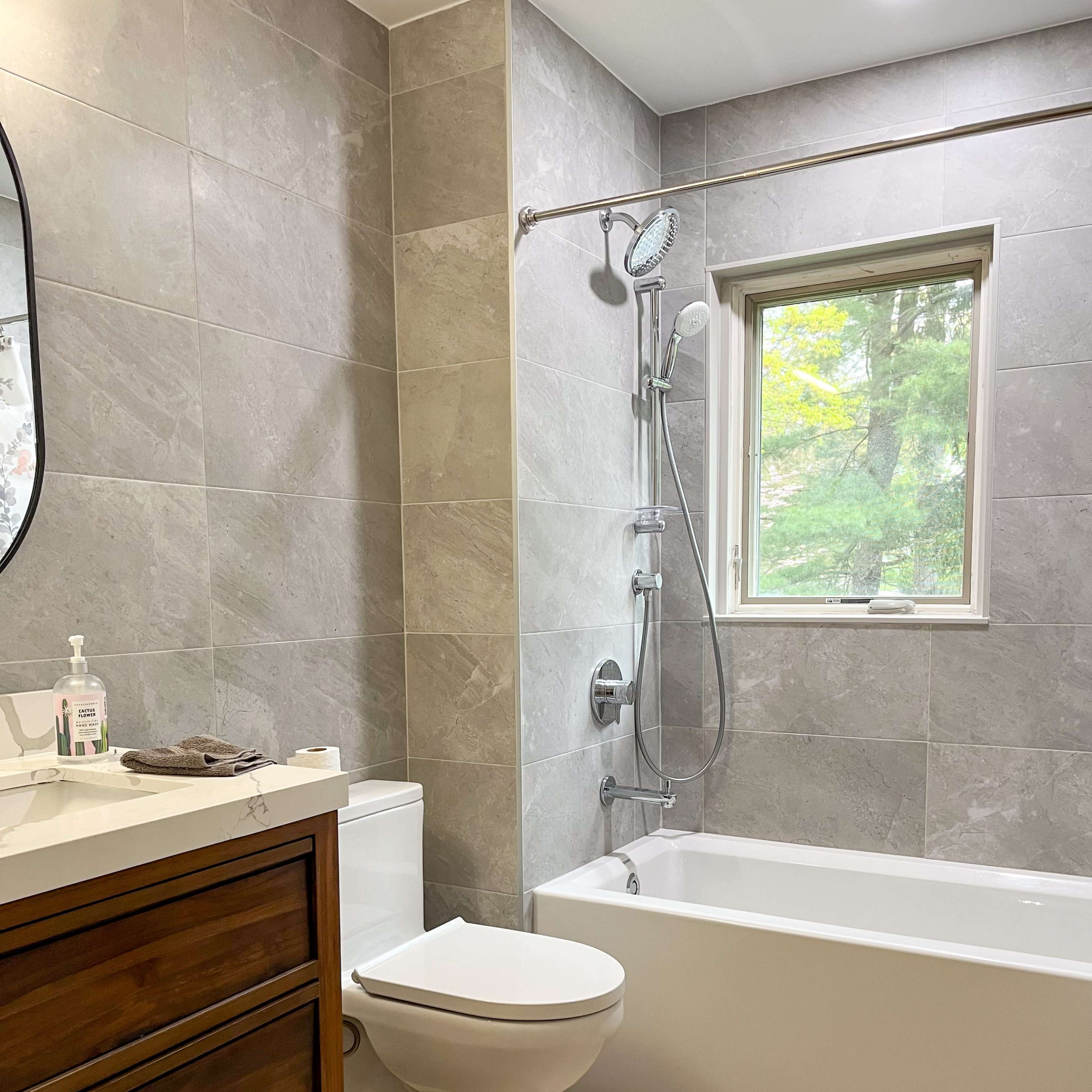 The bathroom features a modern design with a bathtub, a toilet, a shower with a handheld fixture, and a wooden vanity with a sink.