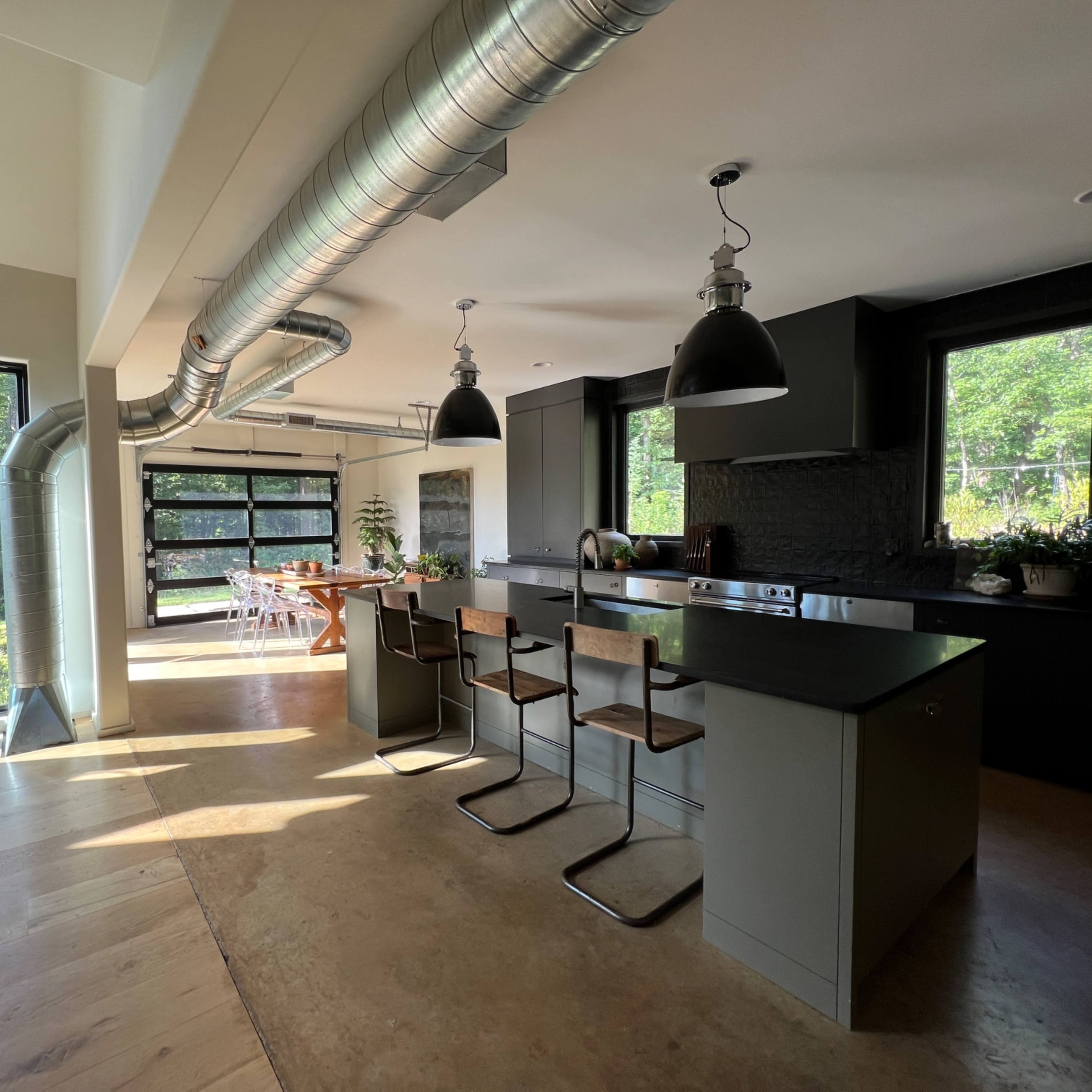 A modern kitchen features a large island with bar seating, sleek cabinetry, and expansive windows overlooking a green outdoor area.
