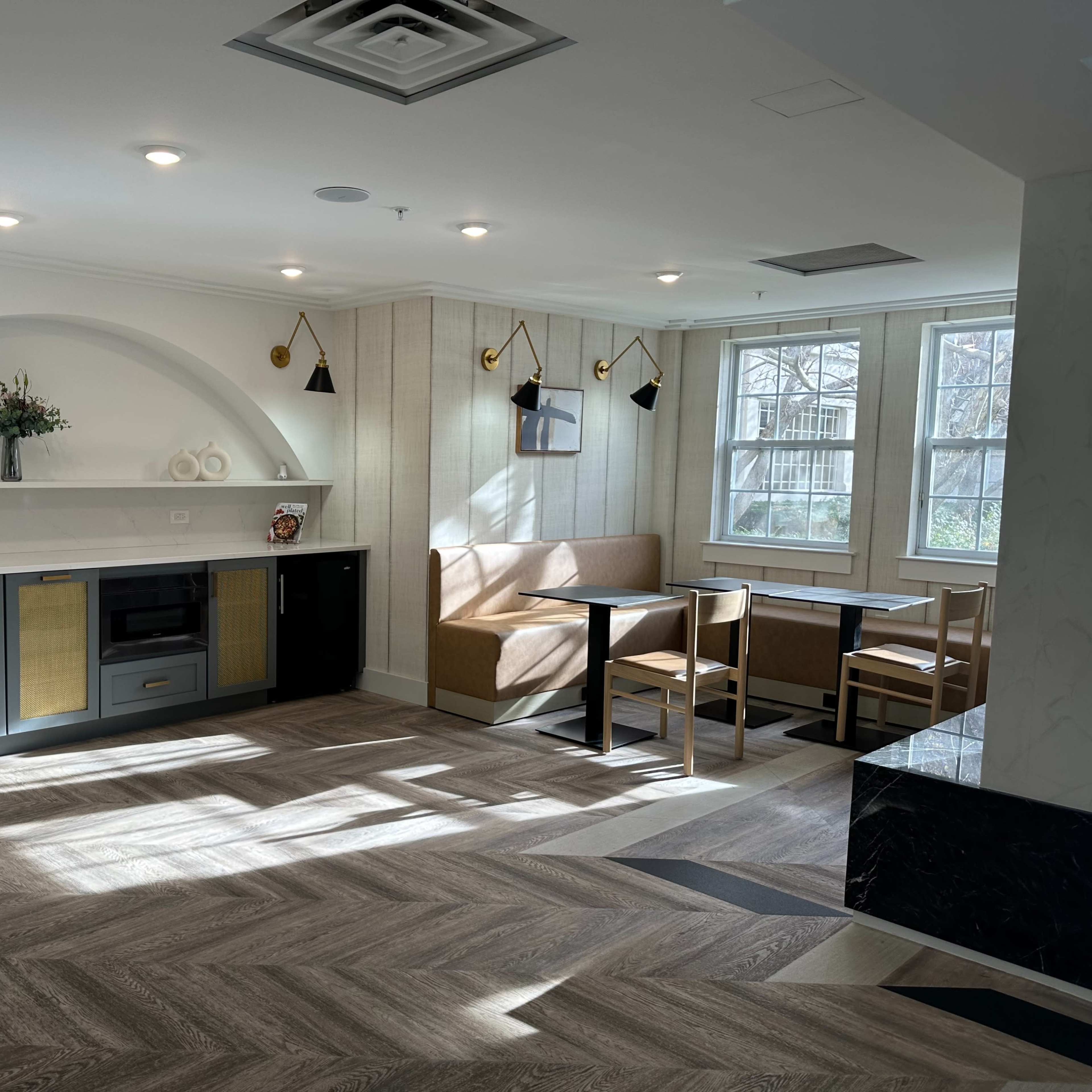 A modern kitchen and dining area with a gray counter, wooden seating, and large windows allowing natural light.
