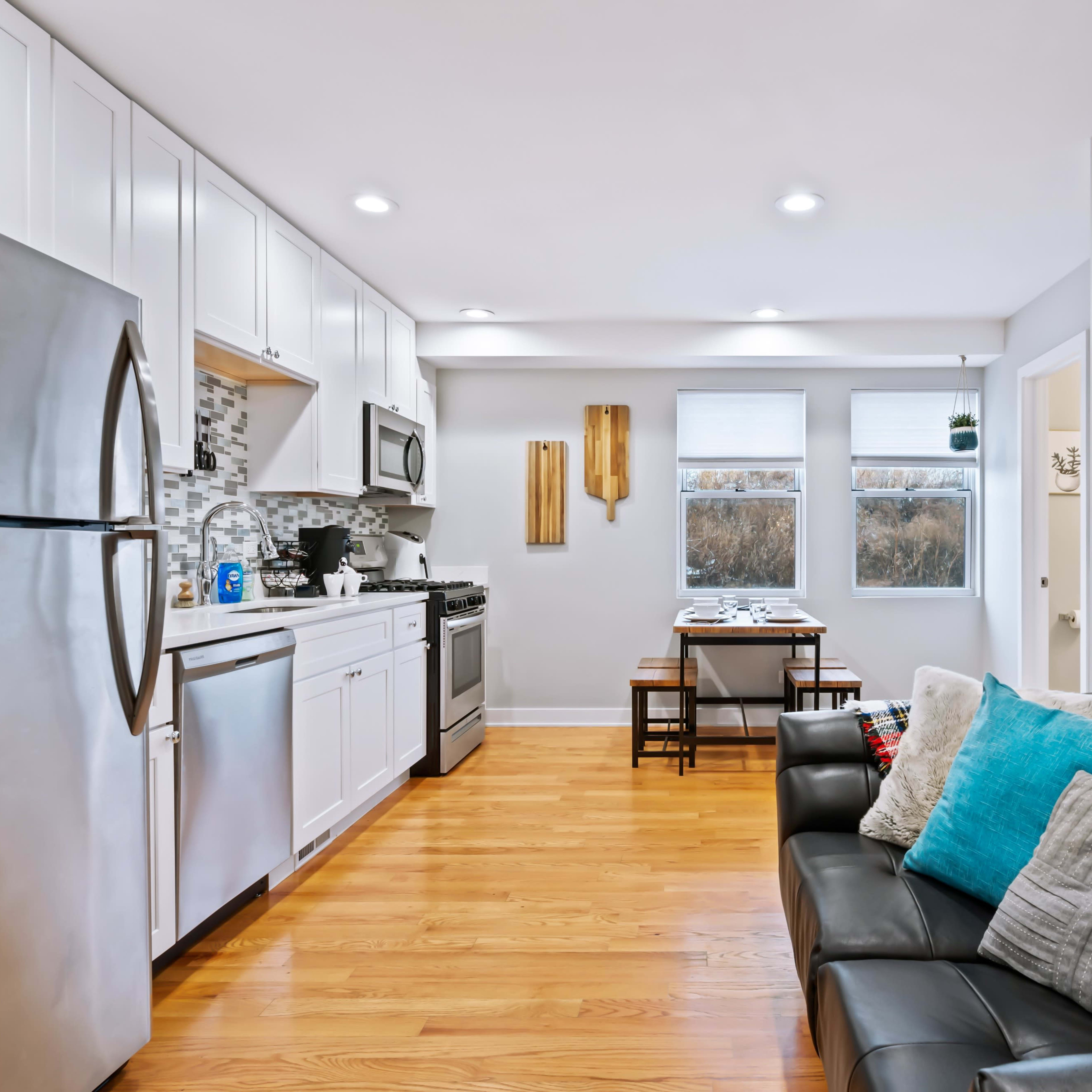 A modern kitchen and living area with stainless steel appliances, wooden flooring, and a small dining table.