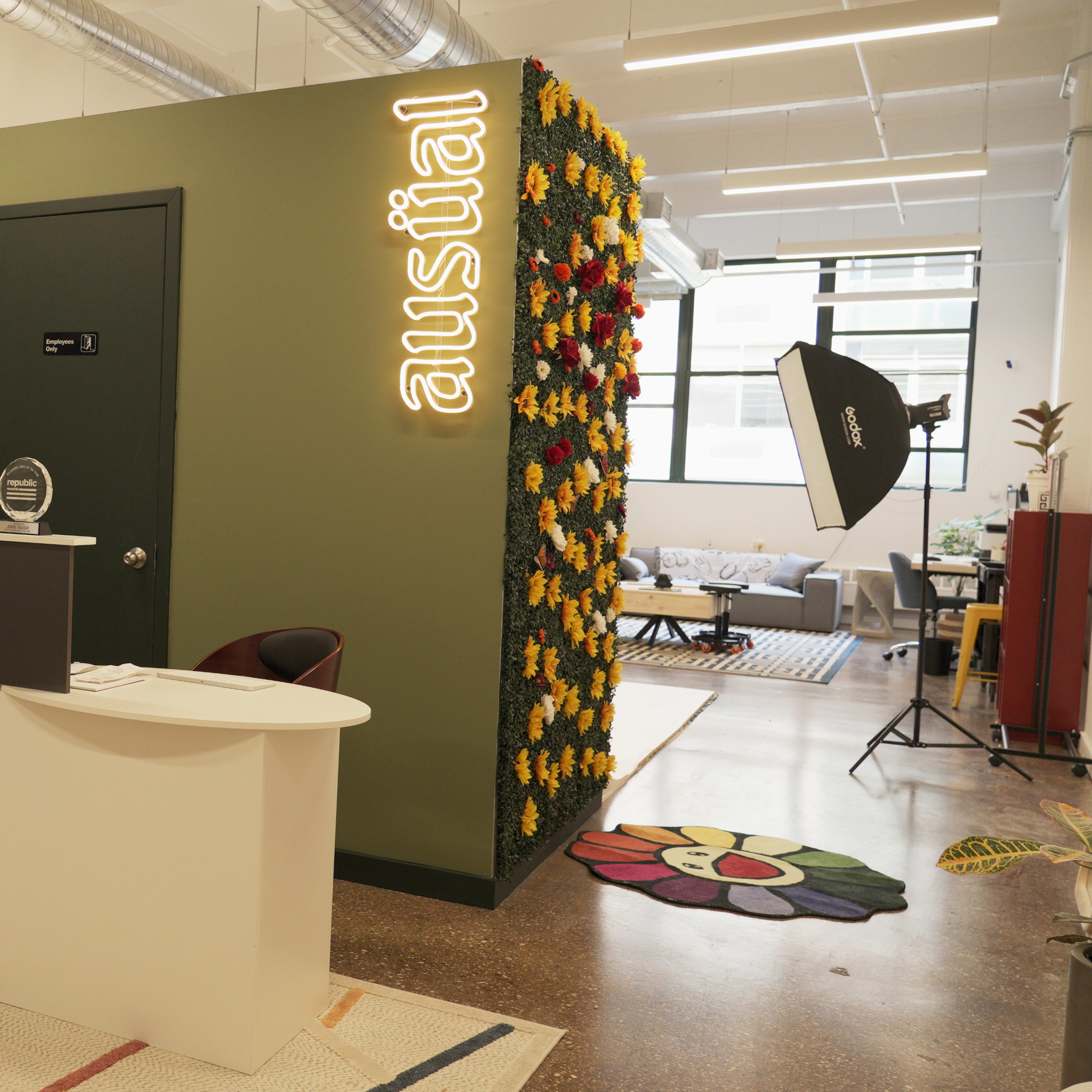 A modern office reception area with a vending machine, a check-in counter, and a wall adorned with flowers next to a lounge area.