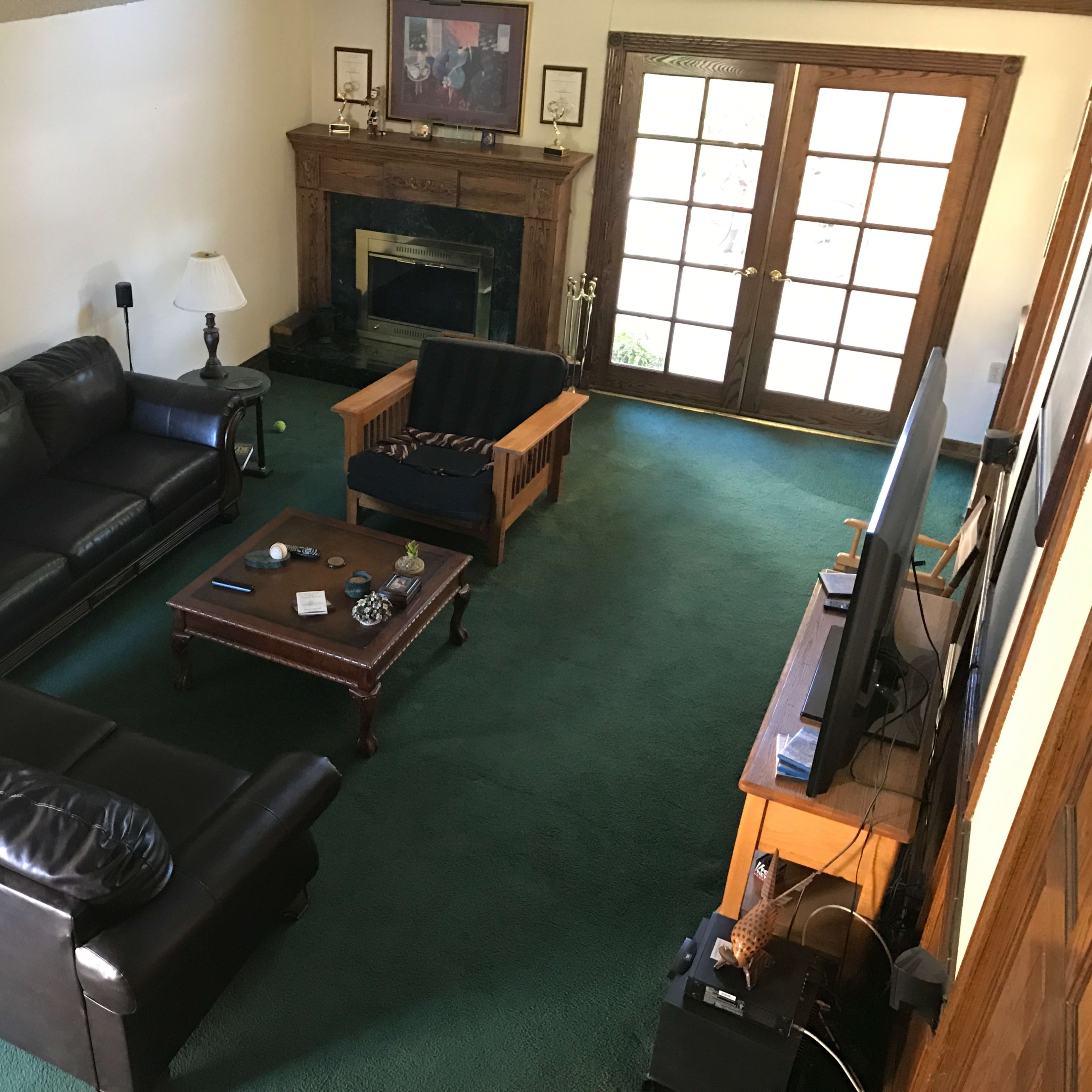 A living room with two black leather sofas, a wooden coffee table, a television, and a fireplace, alongside large patio doors leading outside.