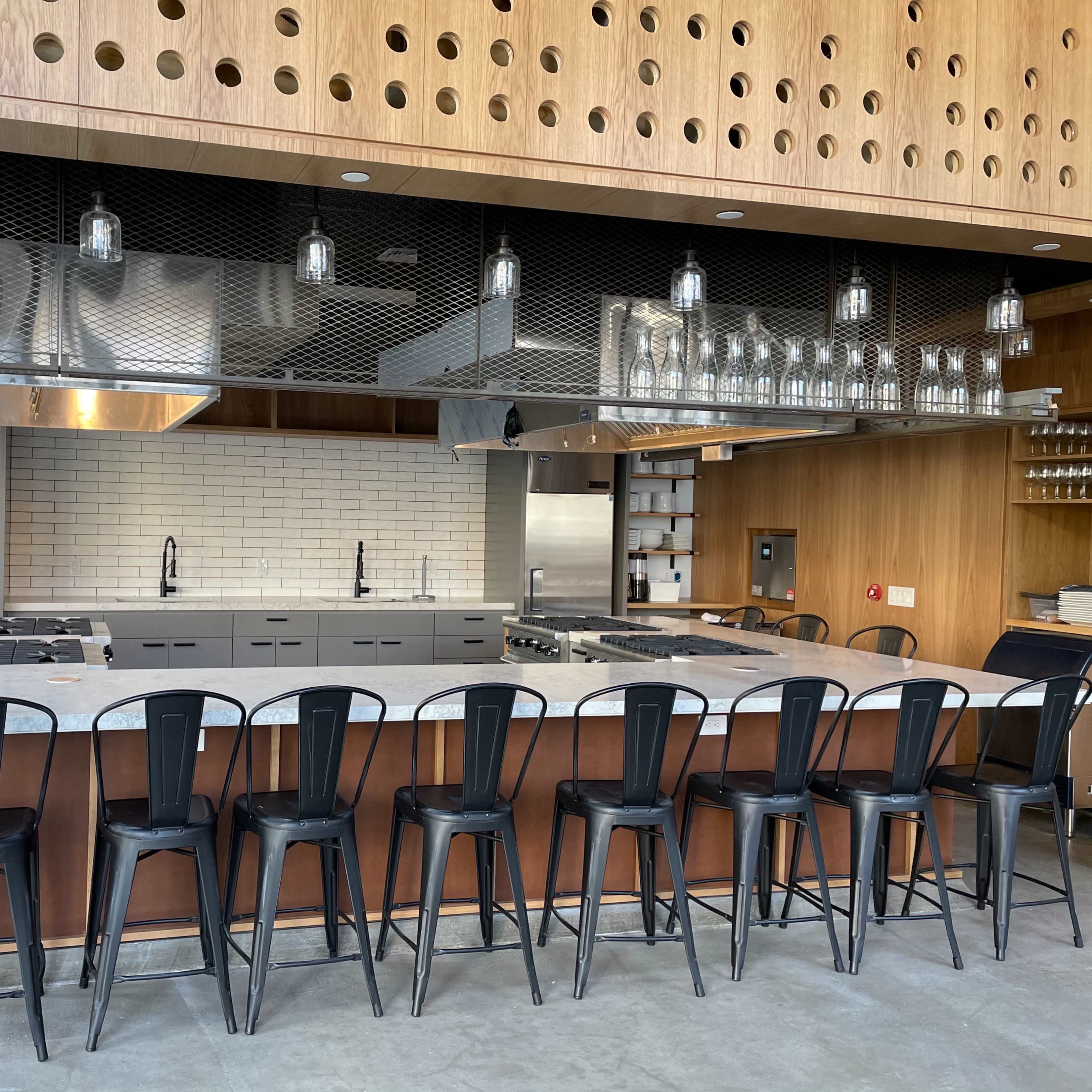 A modern kitchen with a large island, stainless steel appliances, and black bar stools arranged in front of it.