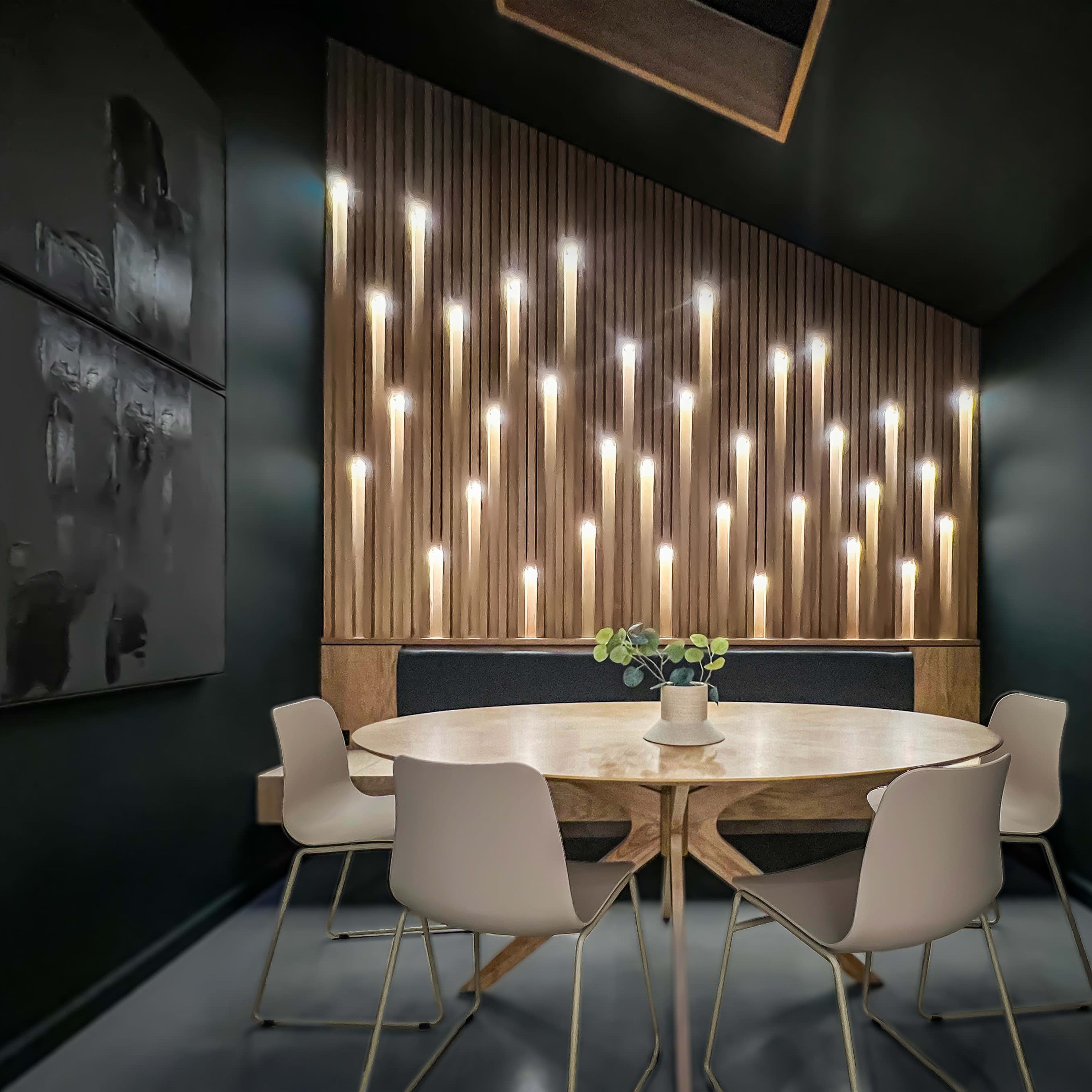 A round wooden table with white chairs is set in a dark room featuring a wall adorned with vertical wooden panels and numerous wall lights.