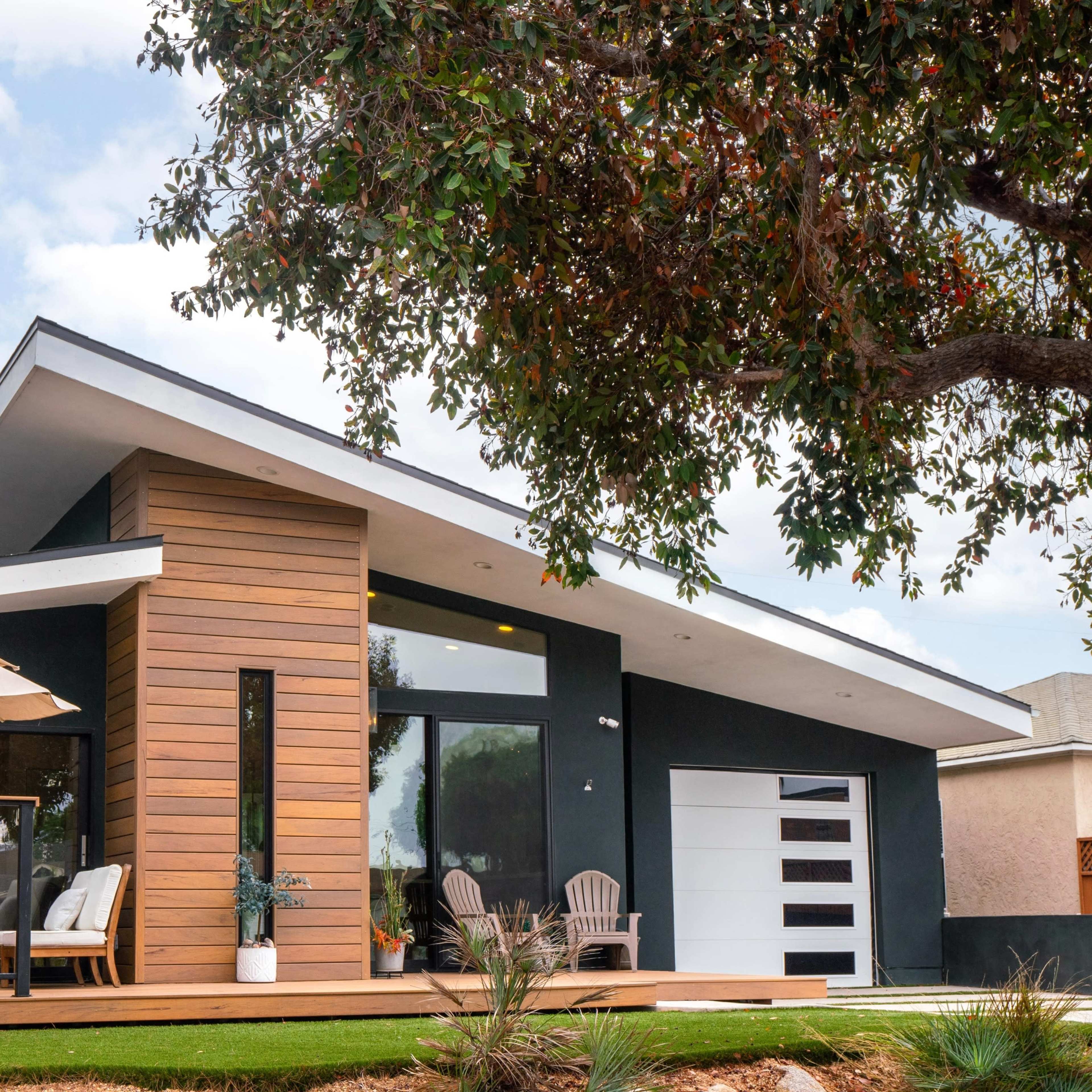 A modern home features a slanted roof, wooden accents, and a patio with an umbrella.