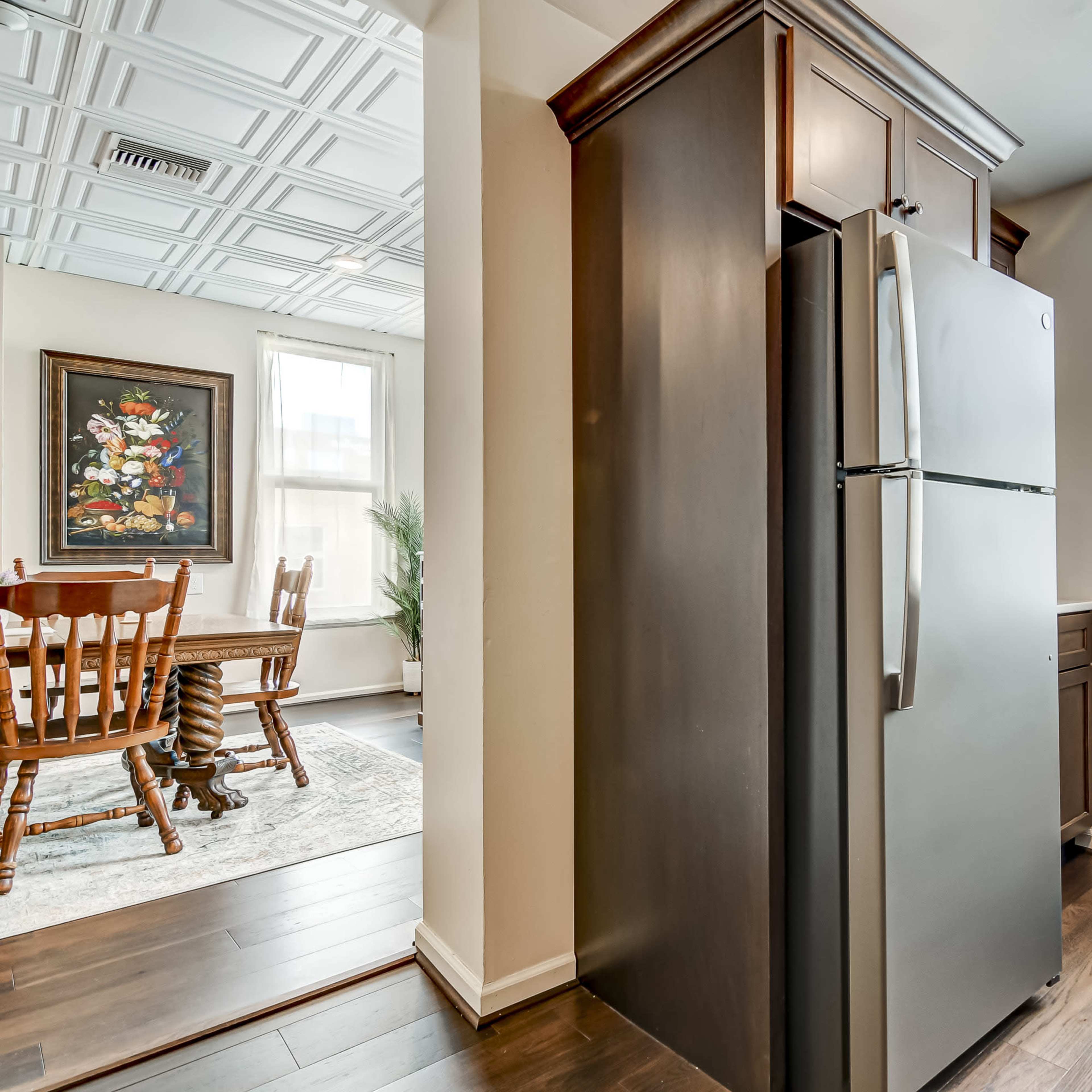 A modern kitchen area featuring a stainless steel refrigerator with wooden cabinetry and a dining area visible in the background.