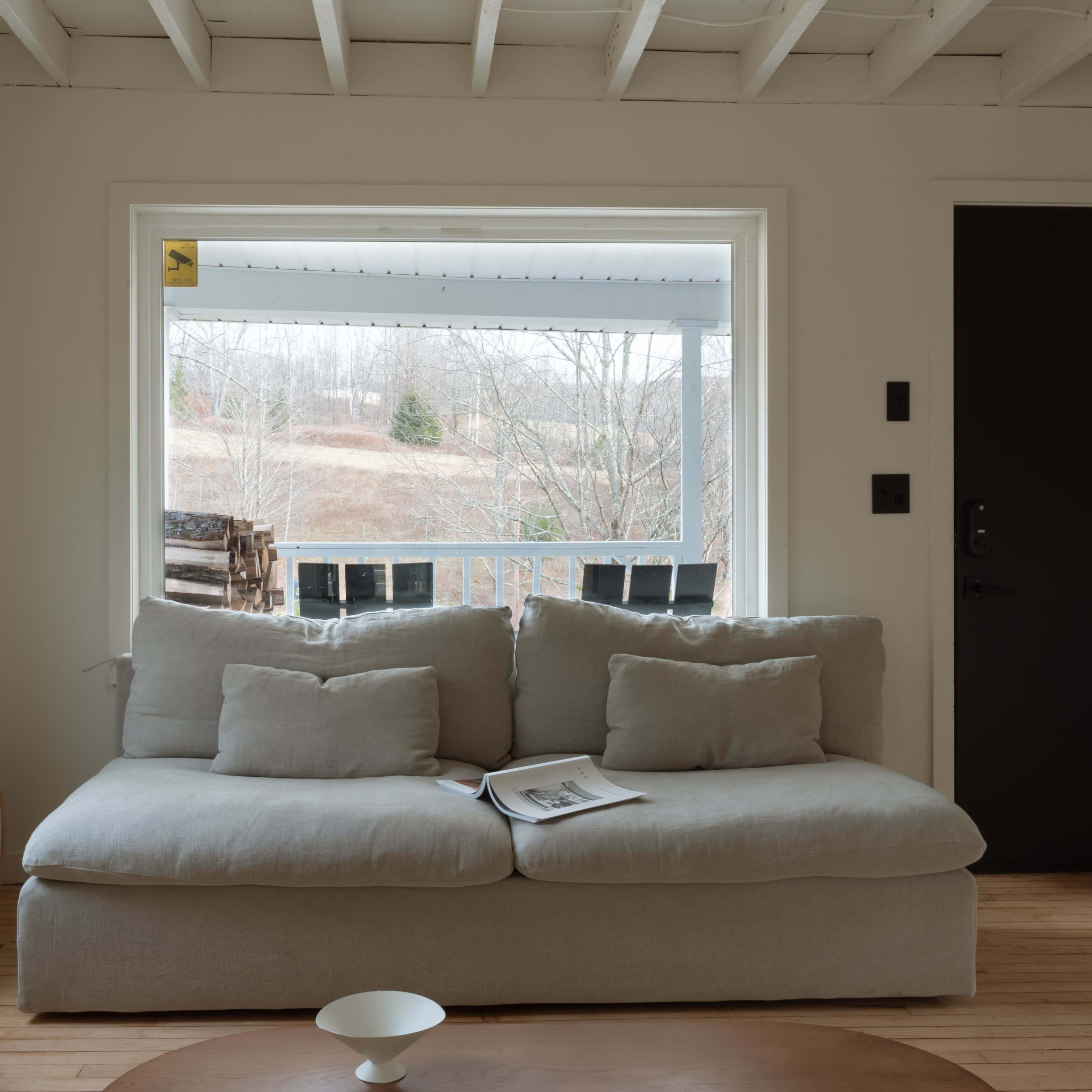 A light-colored living room with a large, comfortable sofa facing a window that overlooks a hillside landscape outside.