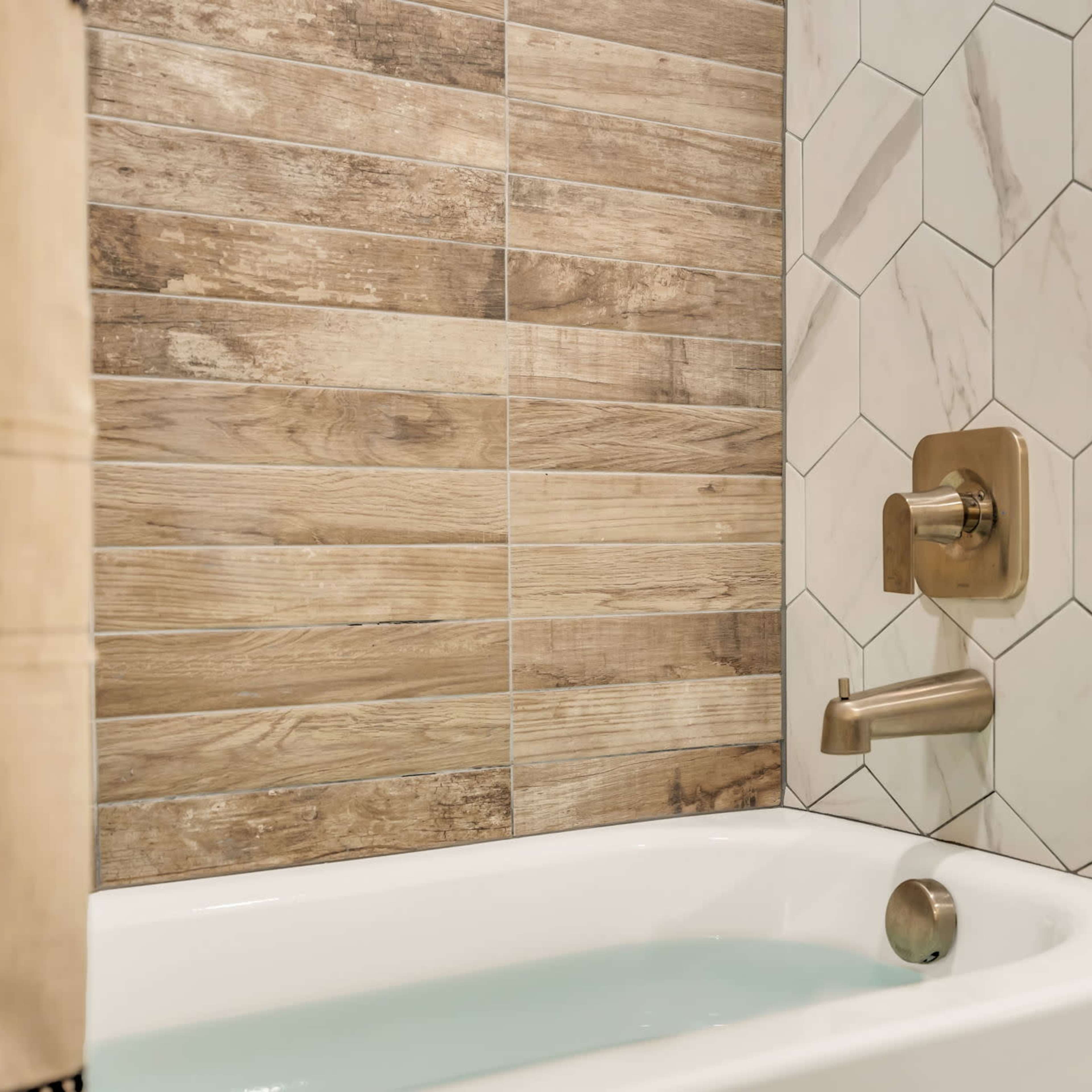 A bathtub with a modern faucet and a wall featuring a combination of wooden and hexagonal tiled designs.