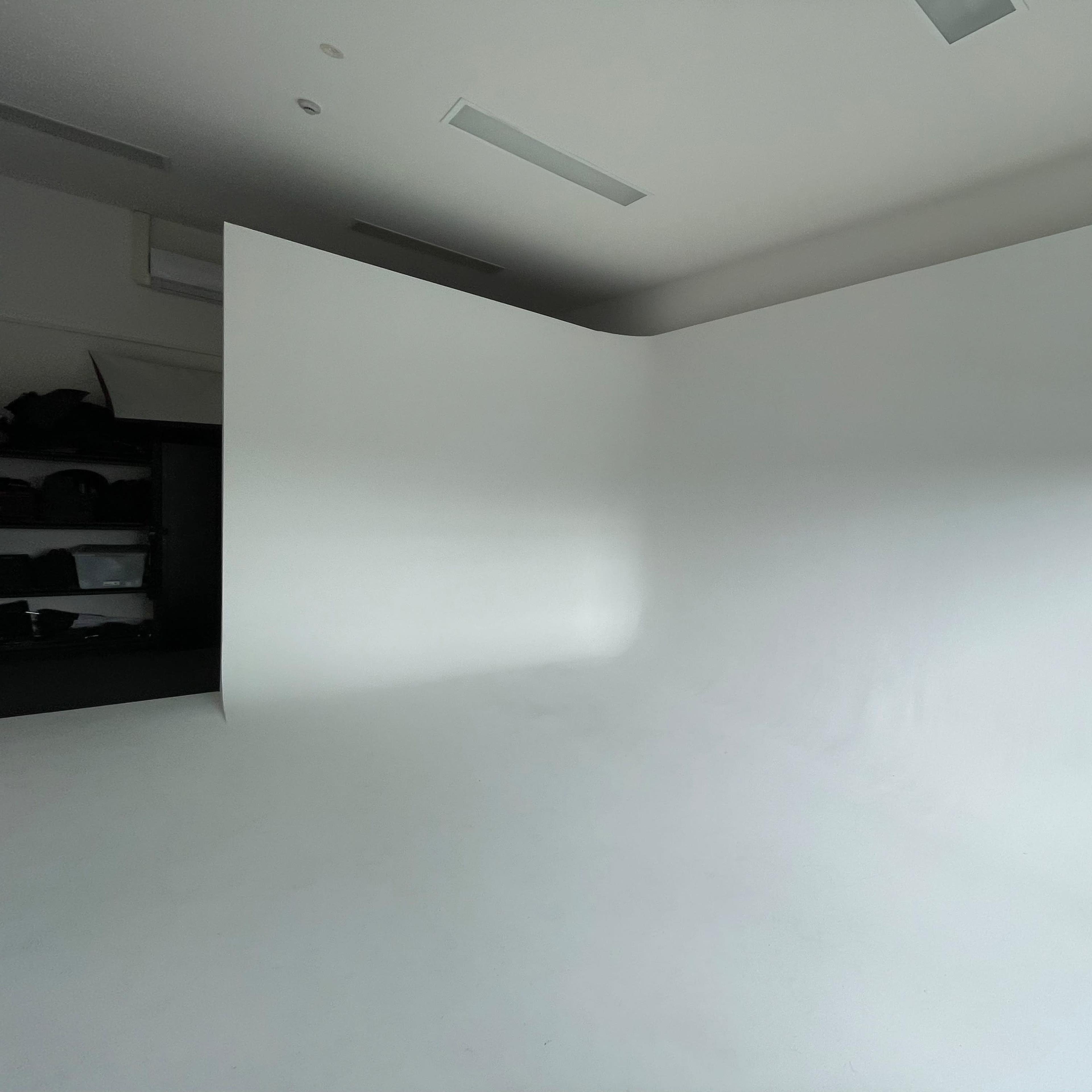 A spacious, empty room with a seamless white backdrop and a partially visible dark storage area in the corner.