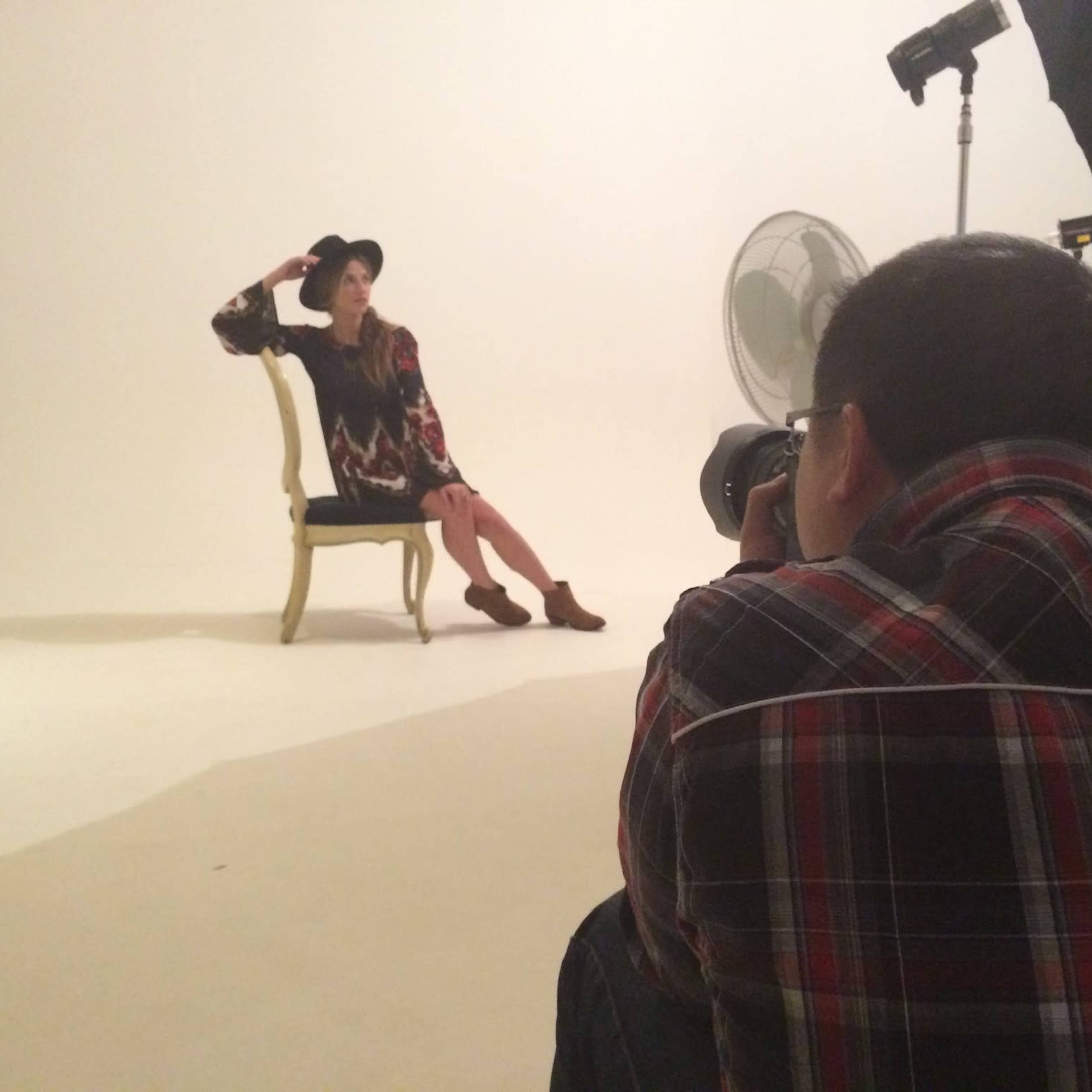 A photographer captures a model seated on a chair in a studio setting.