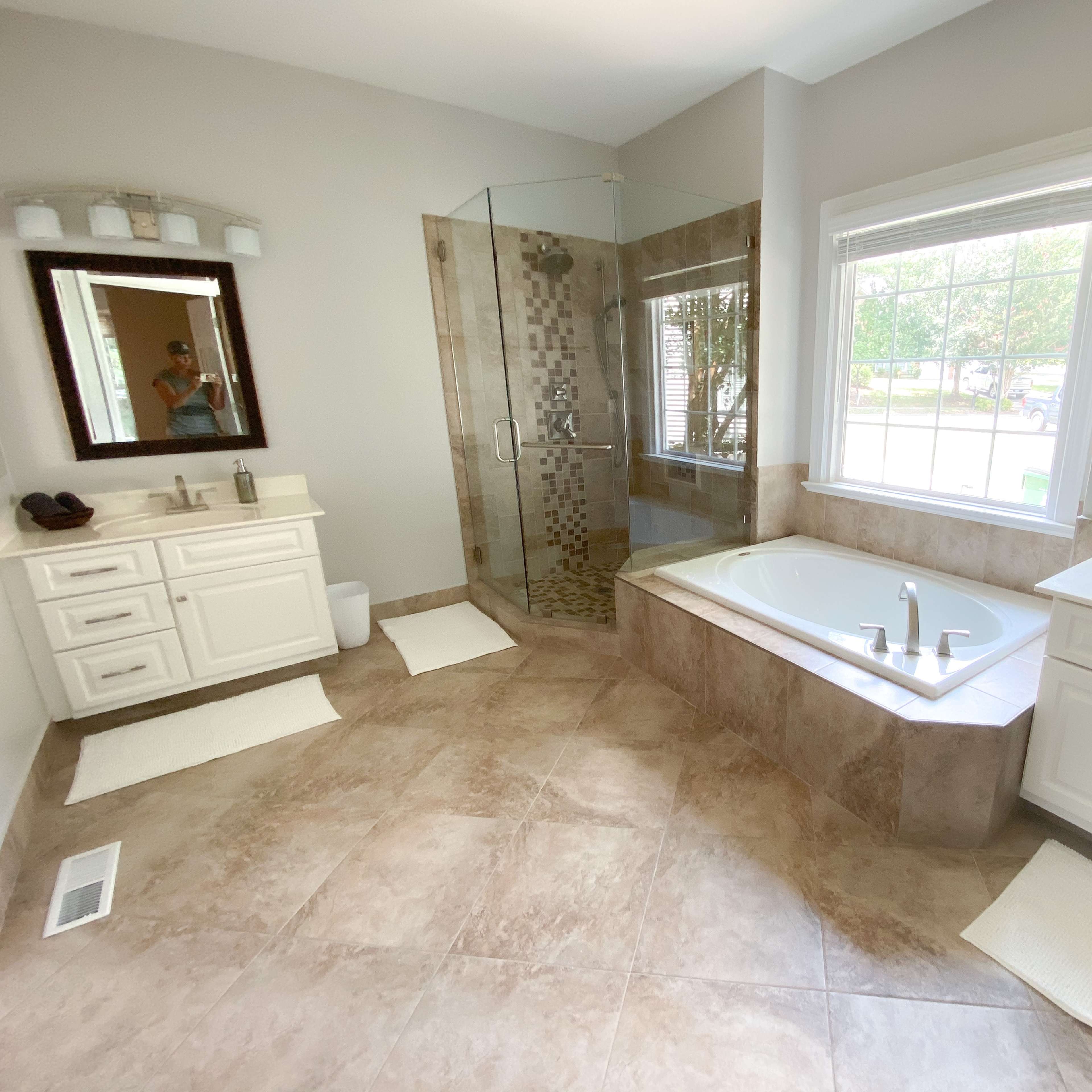 A spacious bathroom features a glass shower, a large tub, double sinks, and natural light from a window.